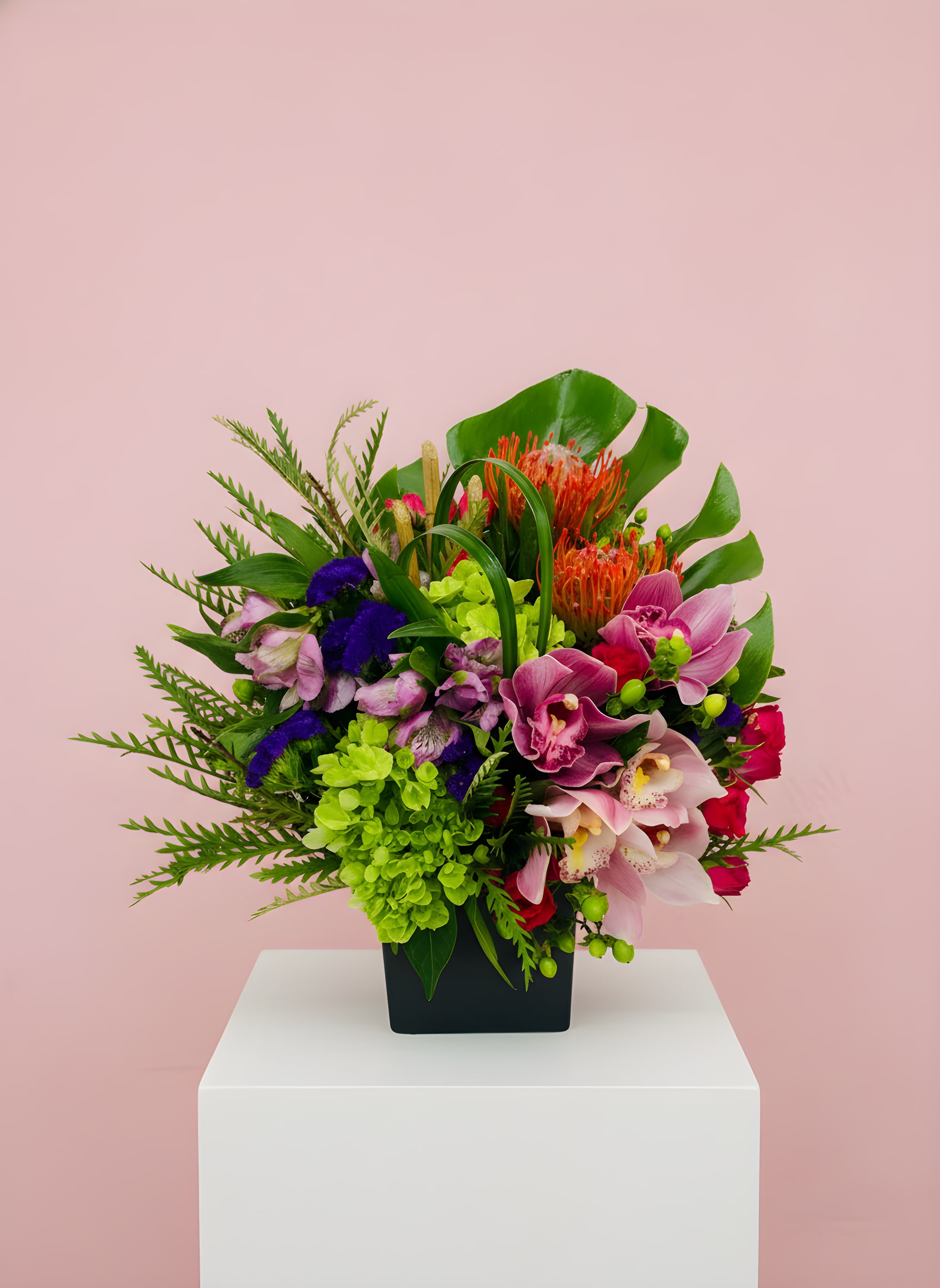 LF94 - Tropical Exotica - An exotic tropical beauty, full of color, so pretty and lush! These seasonal topicals, cymbidium orchids, pin cushion protea, hydrangeas and purple status mixed with exotic greens are sure to delight this lucky recipient. Delivered in a black square 5x5 ceramic vase.  15 1/2" H X 13 1/2" W Orientation: One-sided 