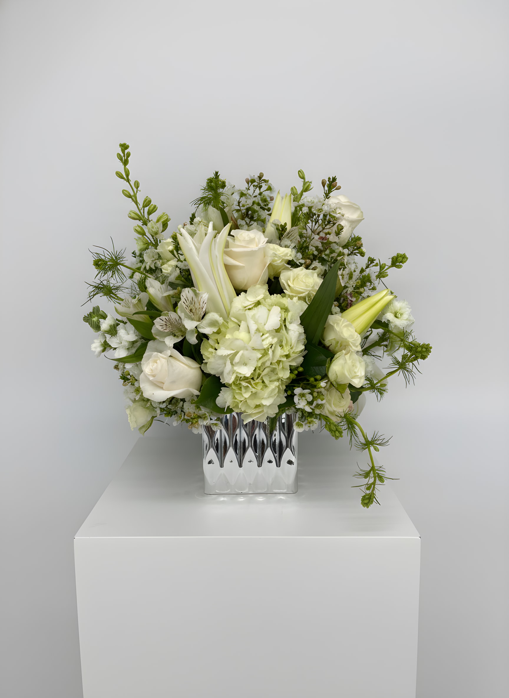 LF24 - Strength and Solace - A beautiful sympathy arrangement in our silver cube vase consisting of an array of white flowers including white lilies, larkspur , roses, spray roses and white alstroemeria . 15 1/2" H  X  13 1/2" W Orientation: all around