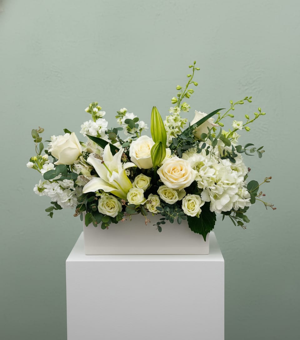 LF133 - Serenity In Bloom - A beautiful arrangement of all white flowers to include lilies, hydrangea, stock, and roses. Peaceful, dignified, and serene.  Orientation - all around  Approx size  20" long X 18" high X 10" deep