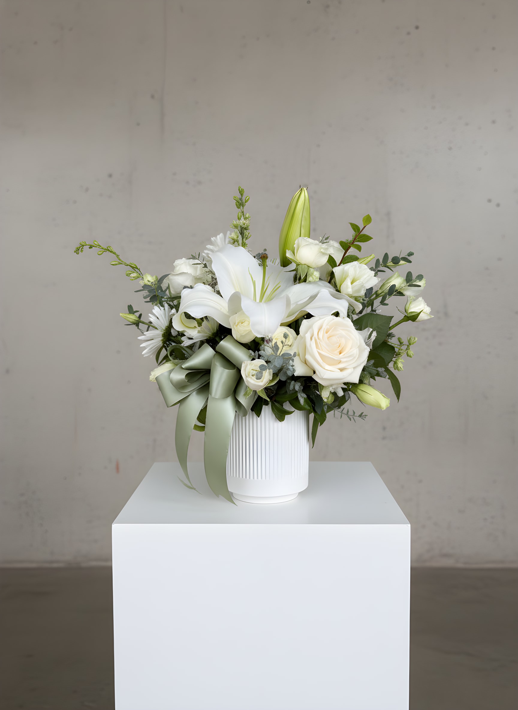 LF31 - Peaceful Comfort - A peaceful gesture that says, "We are thinking of you." Lush white roses, stock, alstroemeria and  other seasonal blooms for a peaceful comforting look.  The beautiful bouquet is nested in a white decorative round vase, and finished with a pretty sage green ribbon. 15 1/2" H  X 13 1/2" W Orientation: All around 
