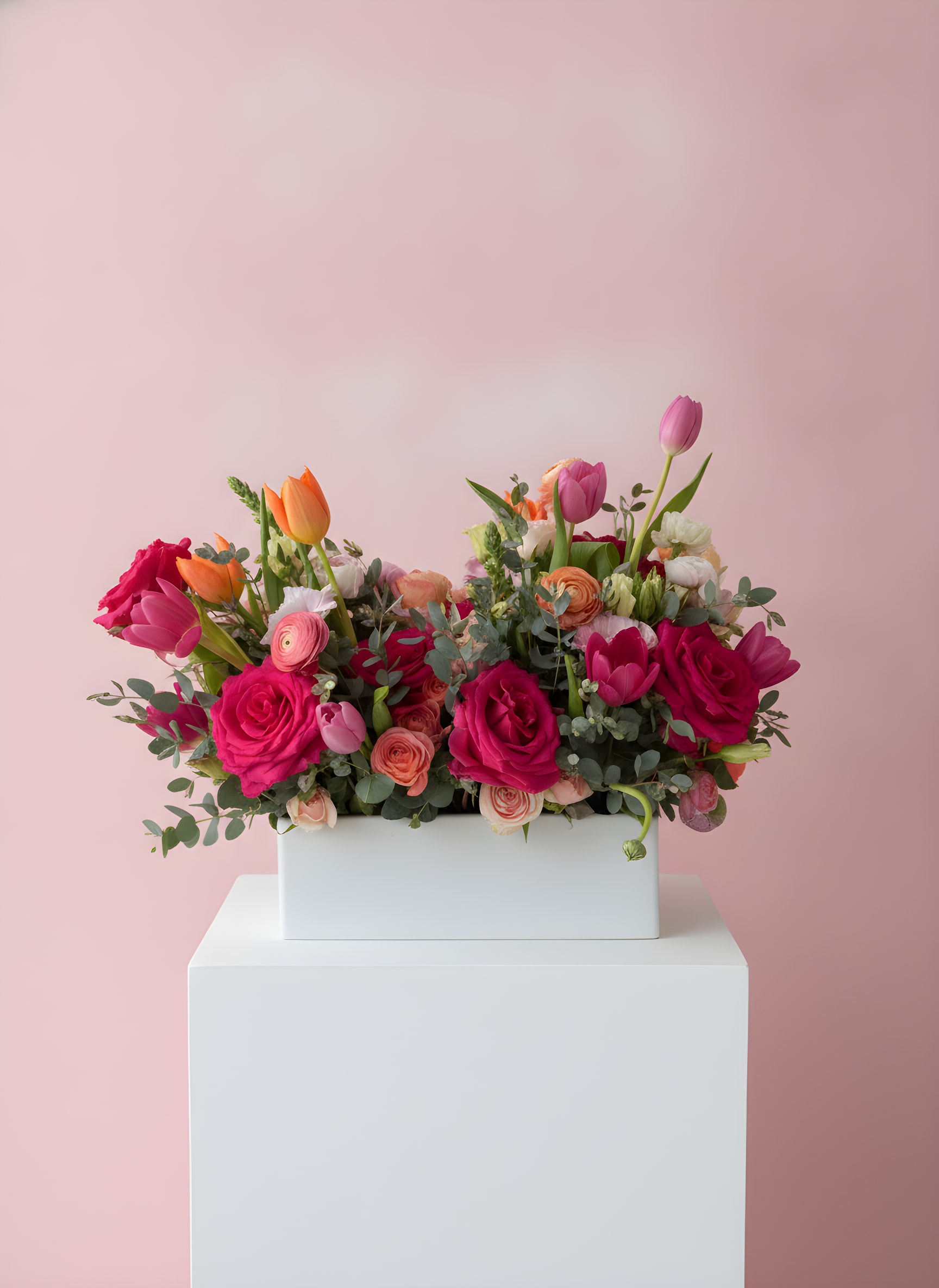 LF425  Blushing Joy - A cheerful and vibrant arrangement bursting with hot pink roses, tulips, ranunculus, and soft peach accents, beautifully gathered in 5x12 inch white ceramic vessel. Designed to brighten any room, this garden-inspired centerpiece radiates joy, warmth and effortless elegance.  Need one day notice for delivery.  Orientation- all around H 18" X W 10" X L 18"