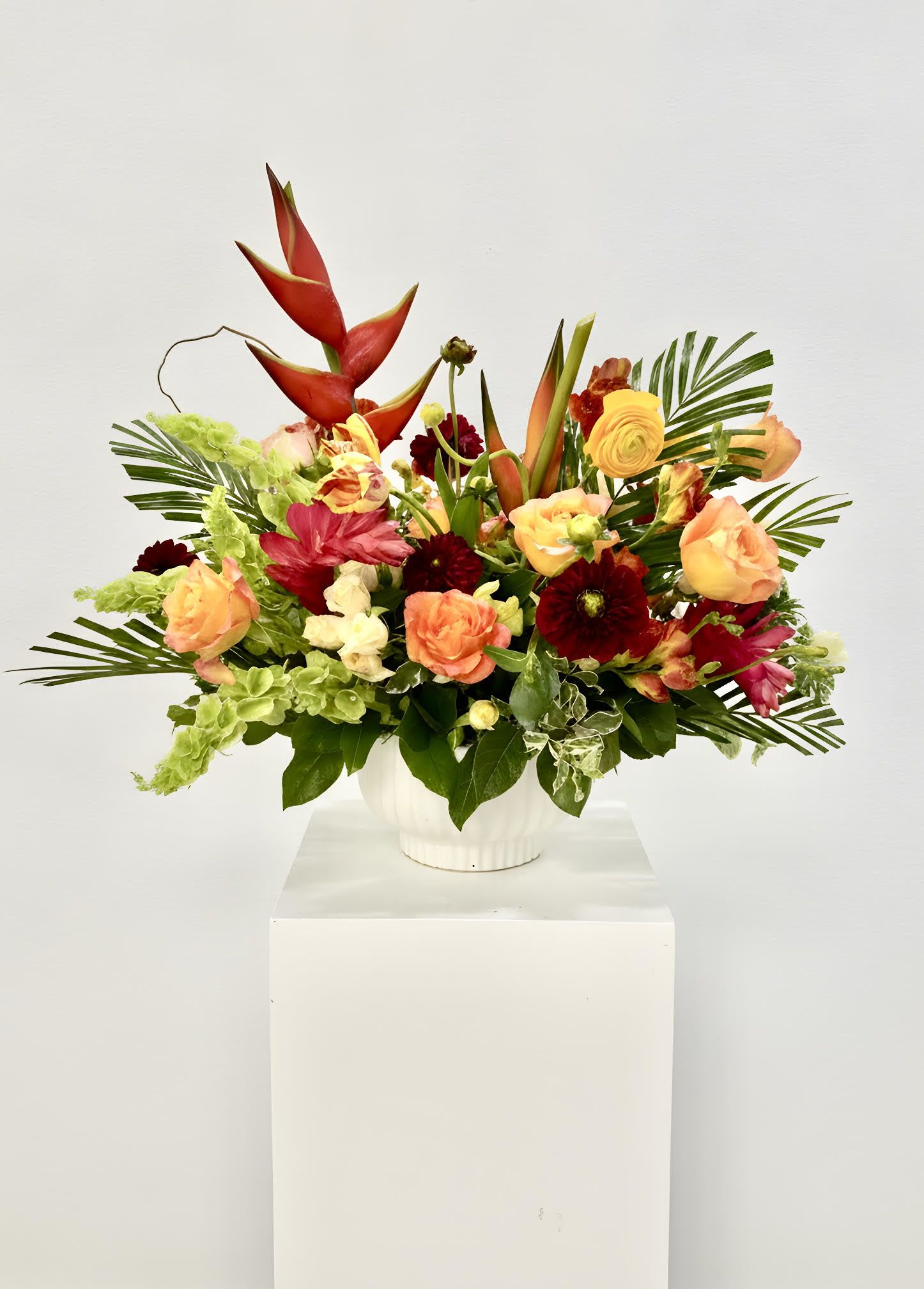 LF426 Tropical Sunset Serenade - A vibrant and artistic arrangement featuring striking tropical blooms, warm peach roses, rich burgundy dahlias, ranunculus  and lush palms and greenery.  Inspired by the colors of a sunset, this cheerful design brings energy, elegance, and a touch of the tropics to any celebration or special occasion.   NOT AVAILABLE FOR SAME DAY DELIVERY    Orientation:  All- Around H 26" X W 24" X L 26"