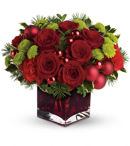 Low red and green arrangement with roses, mums, and ornaments in a red glass cube vase