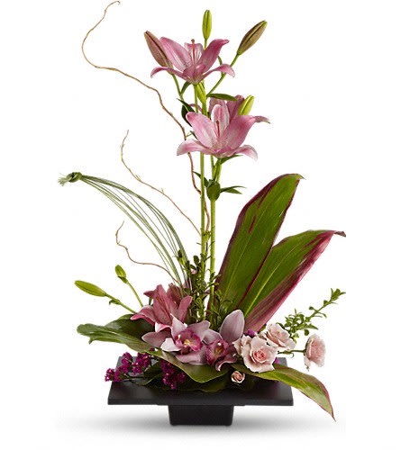 Modern arrangement of pink lilies, orchids, and roses with large leaves in a low black container.