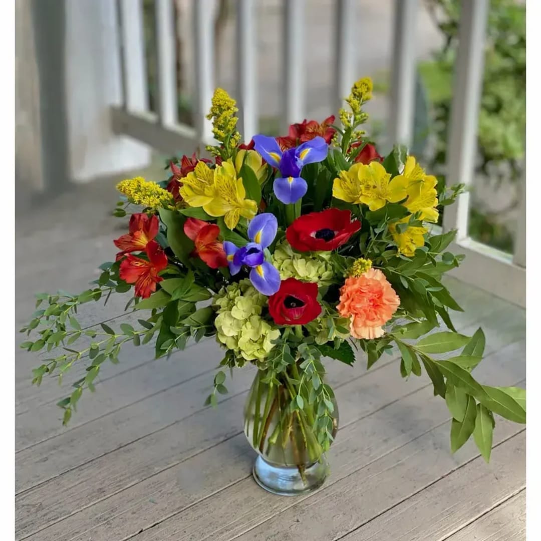 Mixed bouquet in a clear glass vase with red, yellow, blue, and peach flowers