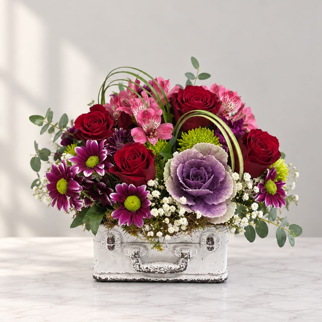Mixed bouquet in a white suitcase-style container with red roses and purple flowers