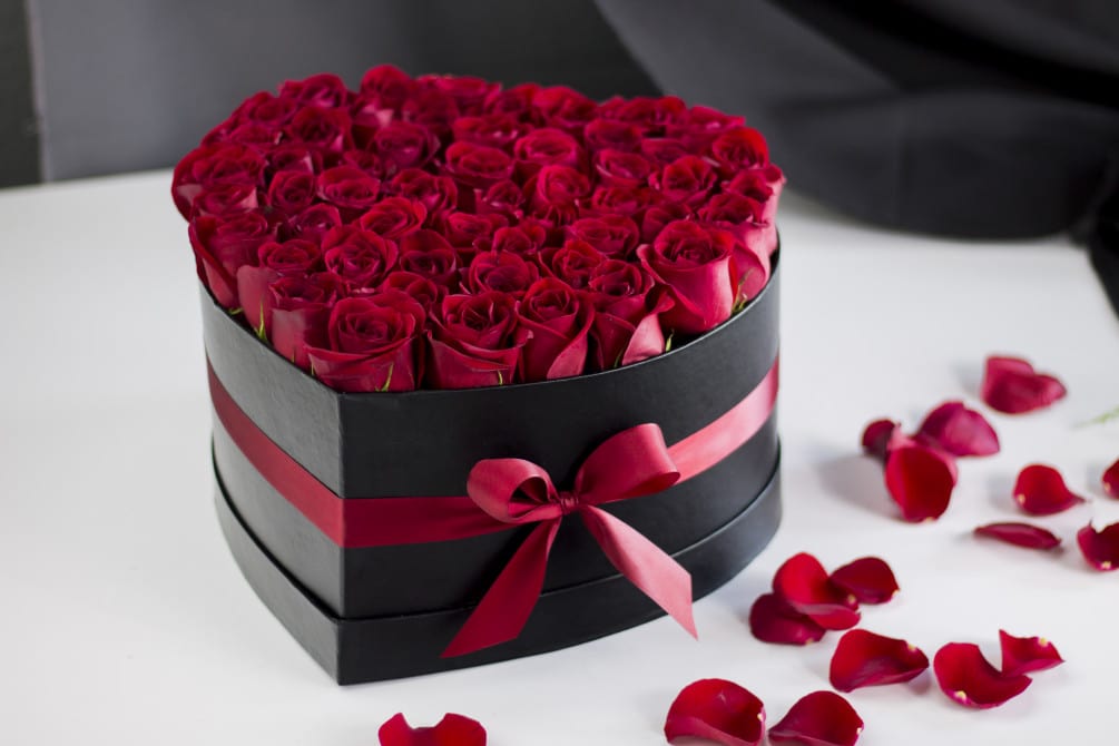 Heart-shaped box filled with red roses and scattered rose petals