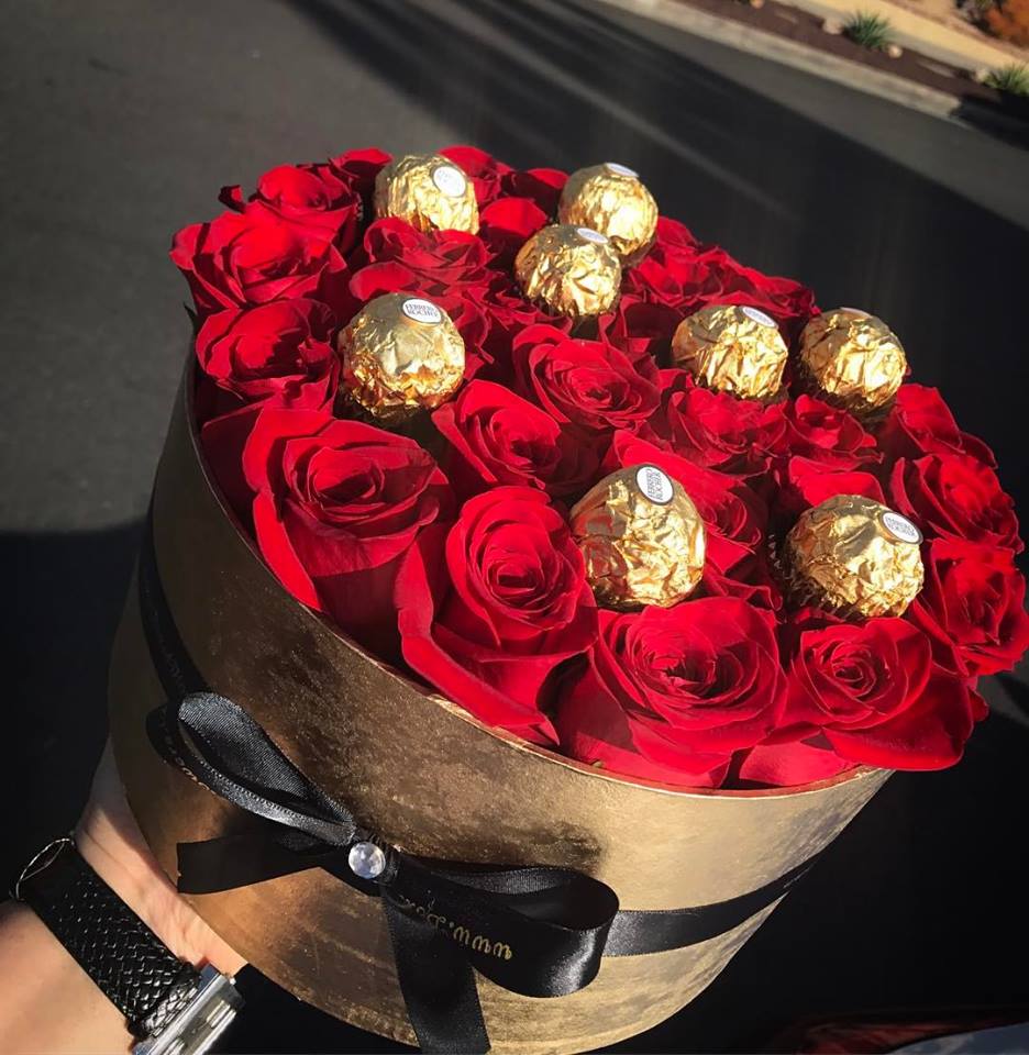 Round box of red roses topped with gold-wrapped chocolates