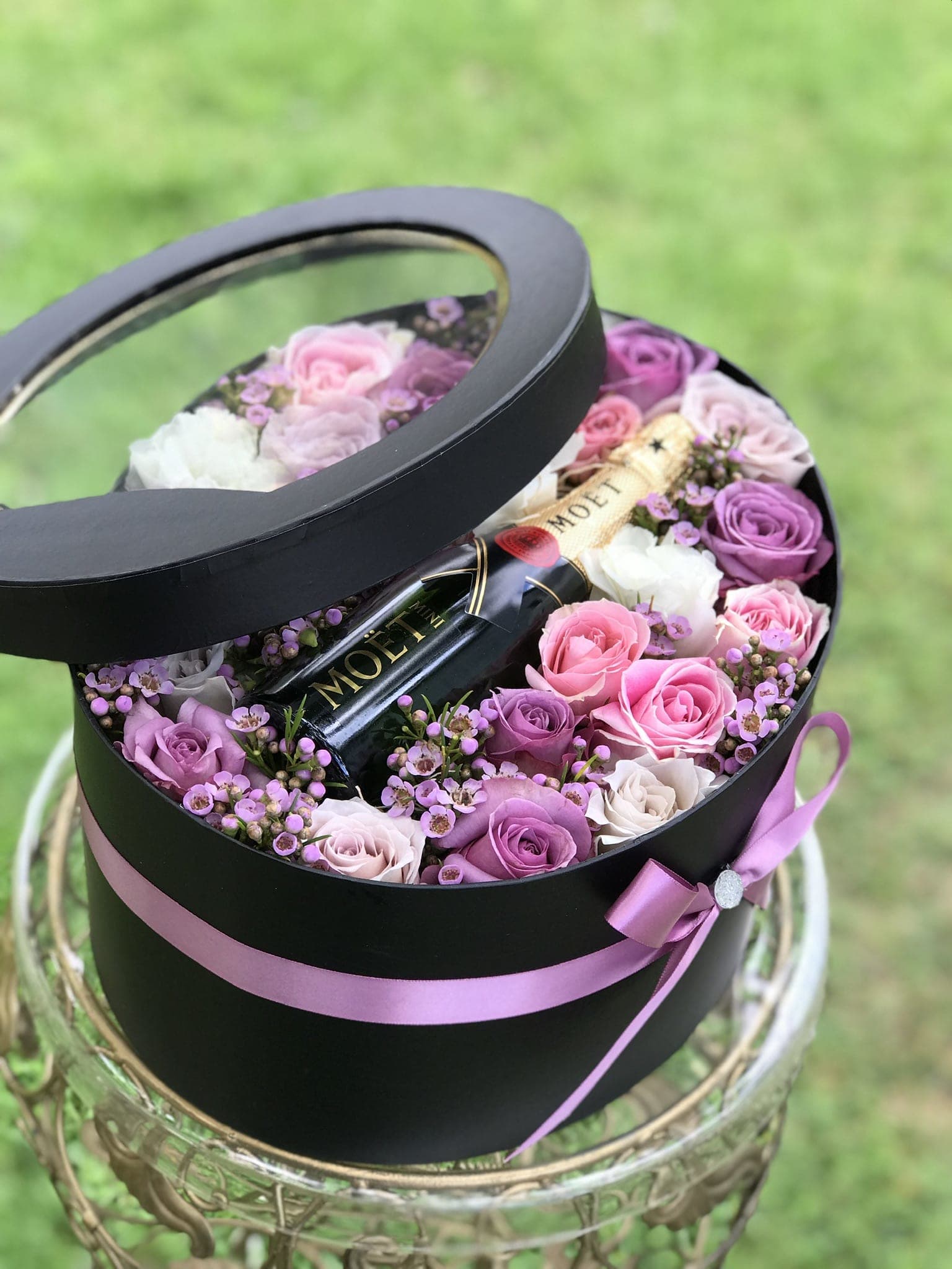 Round black gift box with pink and purple roses and a champagne bottle