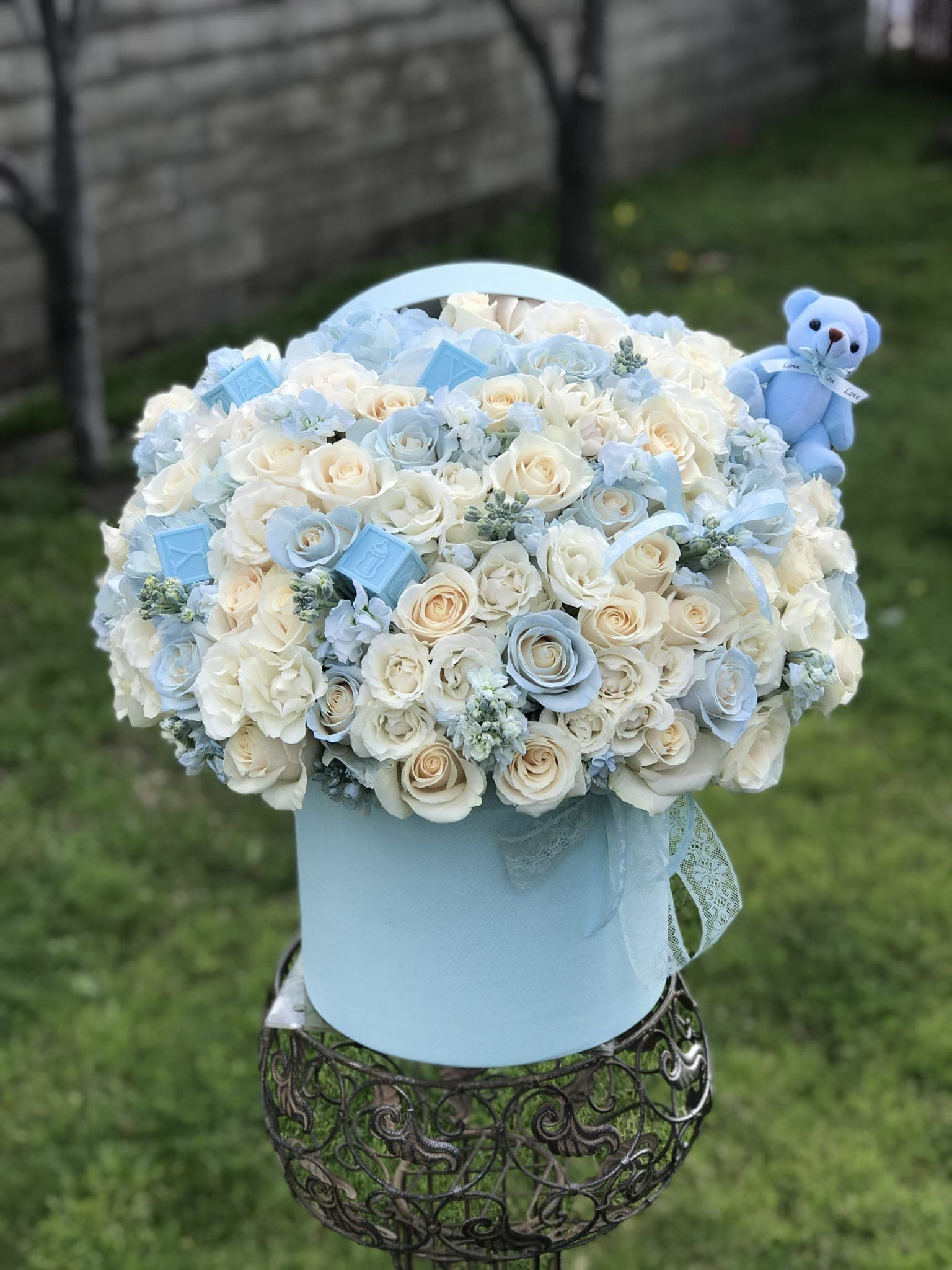 Blue and white rose arrangement in a round hatbox with a teddy bear