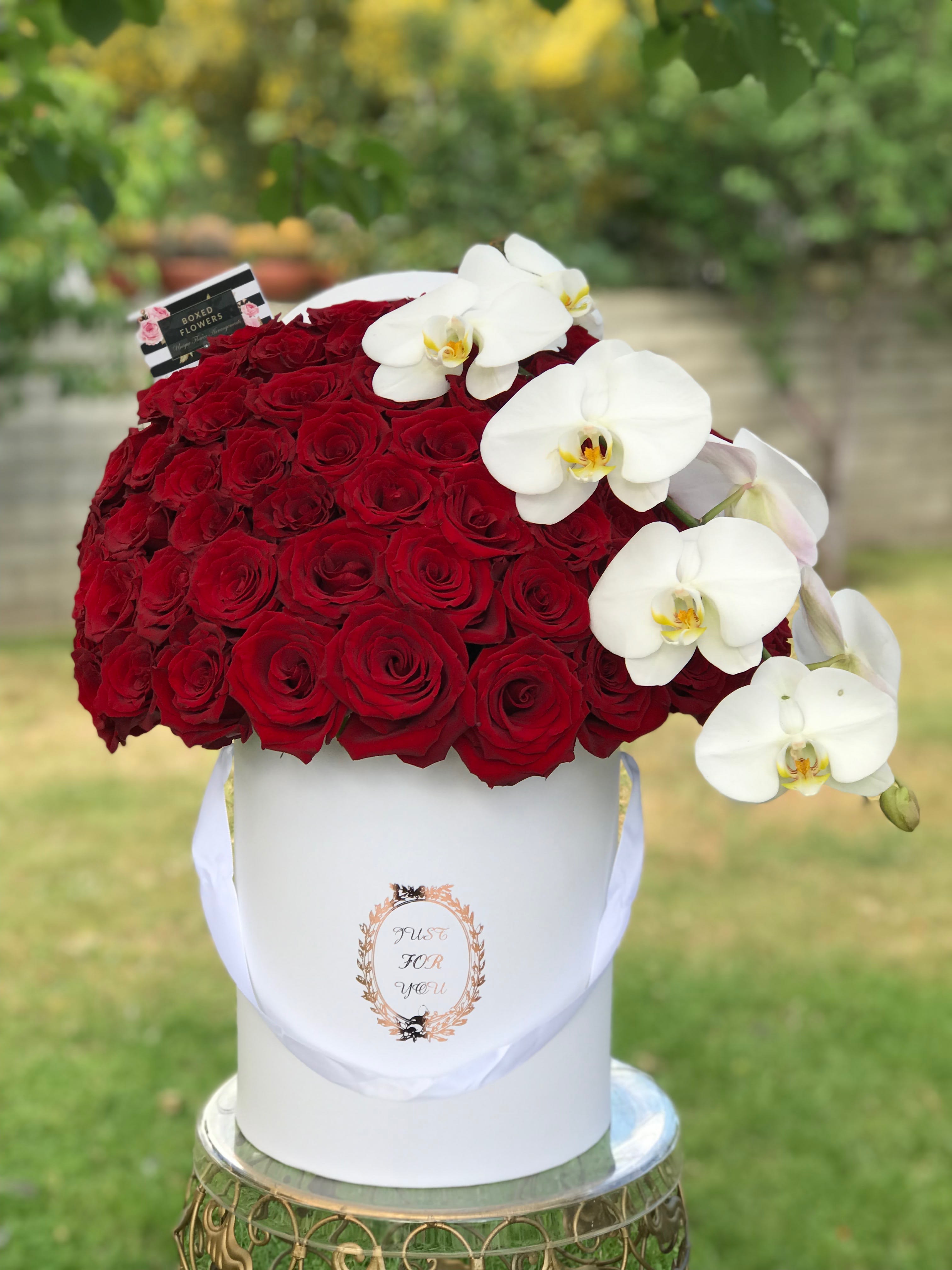 Red roses in a white hatbox with white orchids draped over the side