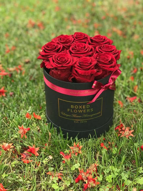 Red roses arranged in a black round box with a pink ribbon