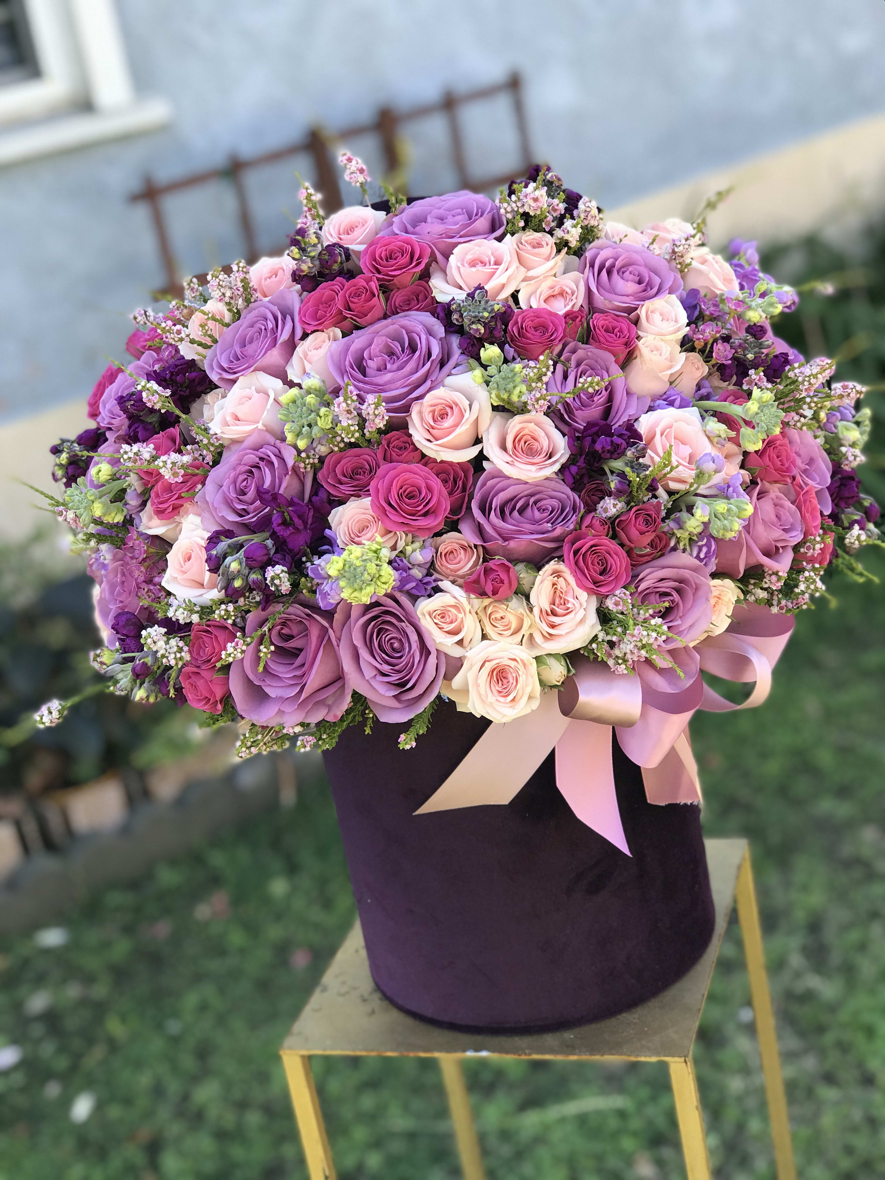 Large bouquet of pink and purple roses in a dark hat box with ribbon
