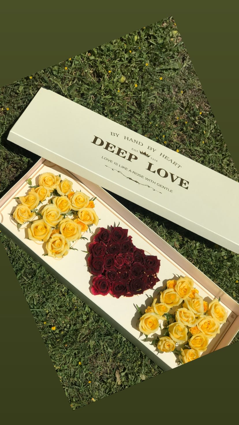 Long box of yellow and burgundy roses on grass
