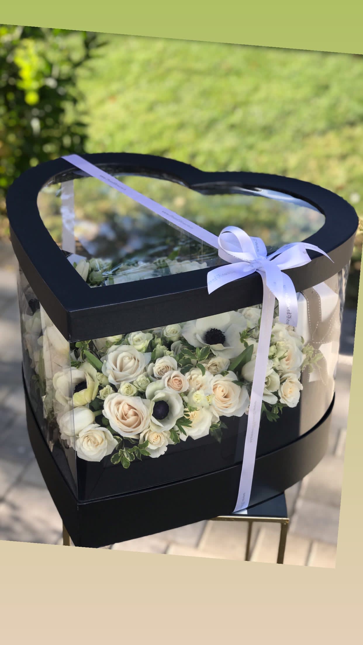Heart-shaped black box with white roses and a ribbon bow
