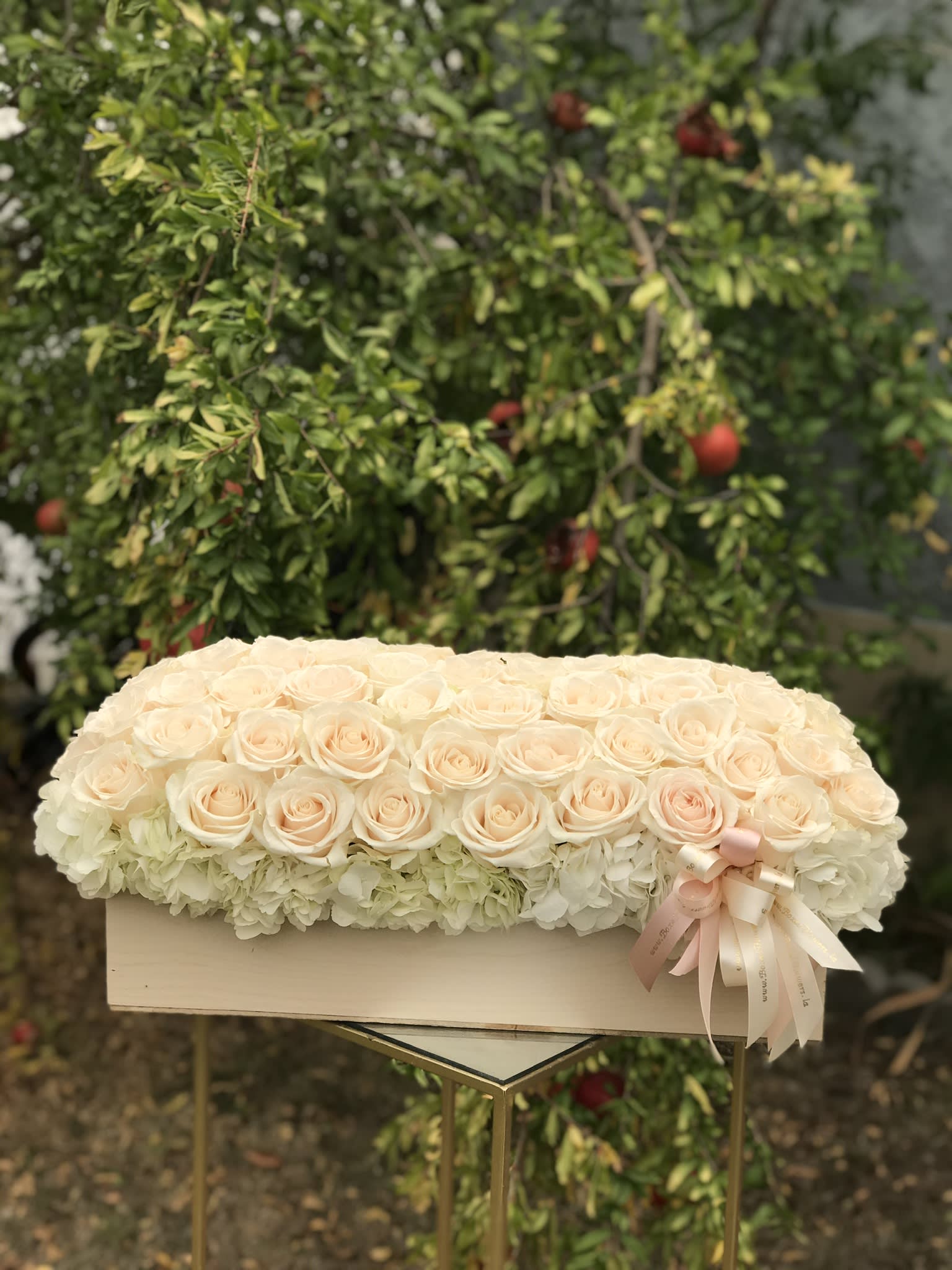 Cream roses arranged over white hydrangeas in a rectangular box with a ribbon bow