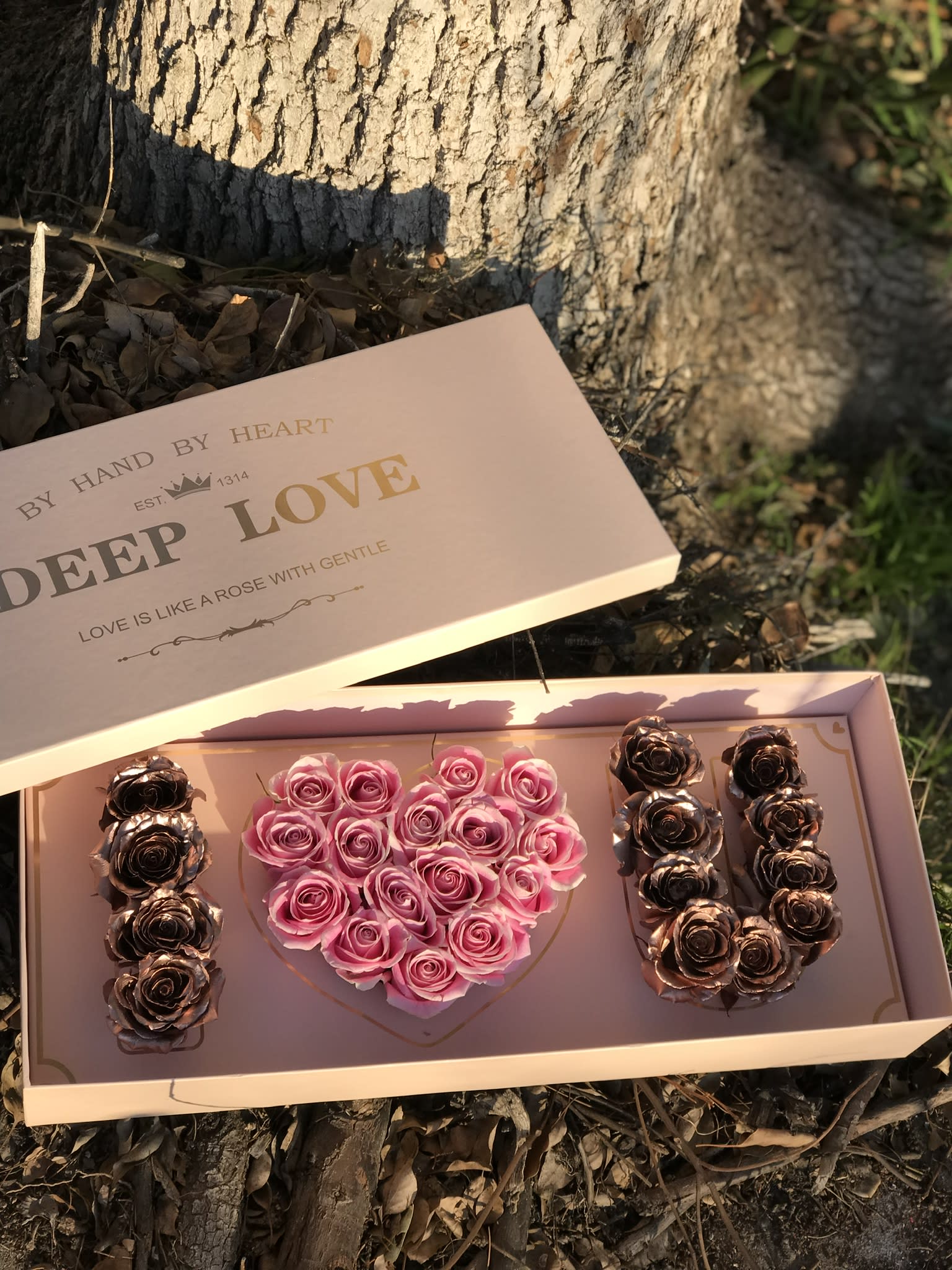 Pink rose arrangement in a heart-shaped box with gold roses on the sides