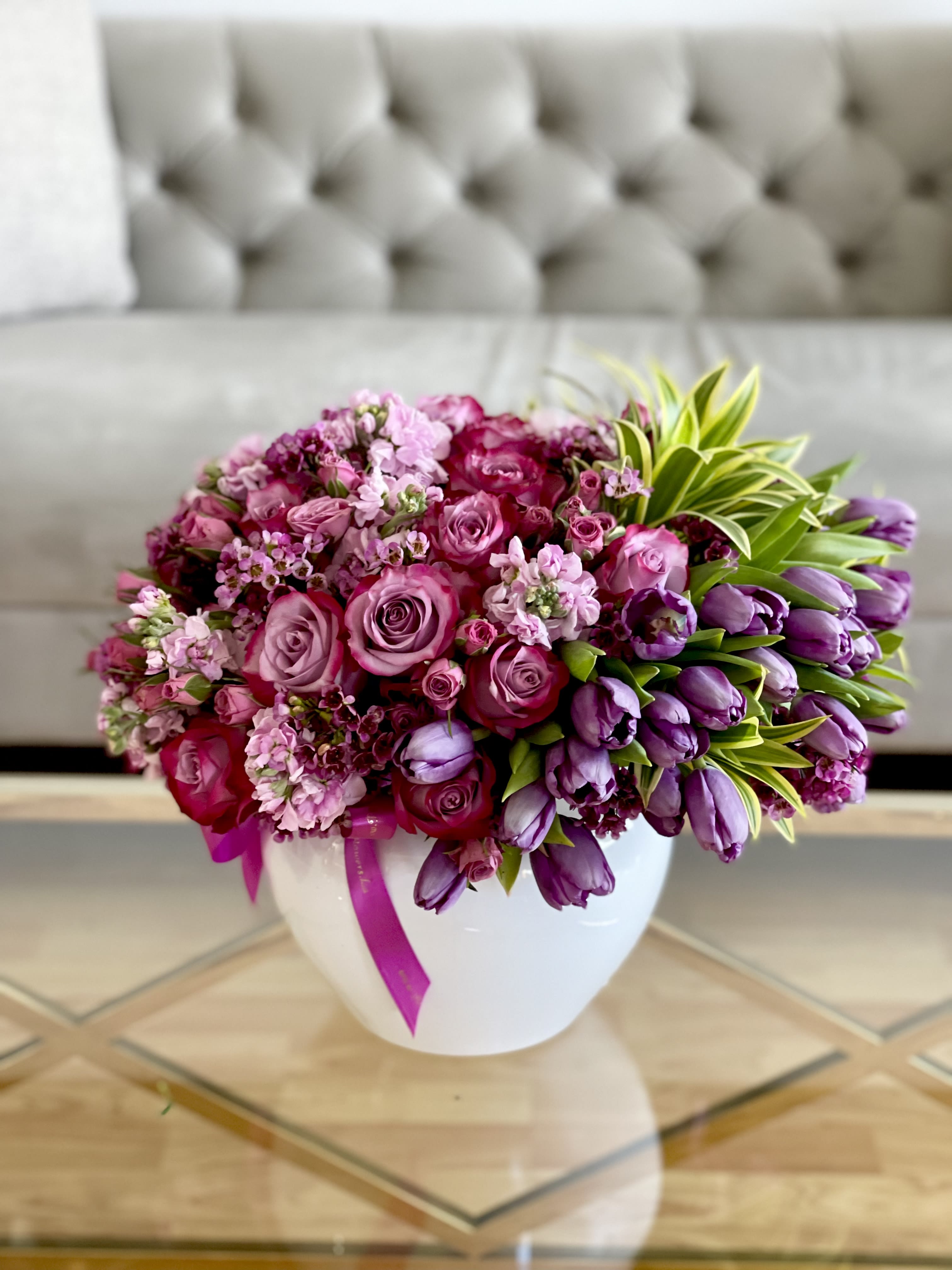 Pink and purple flower arrangement in a white vase with a ribbon