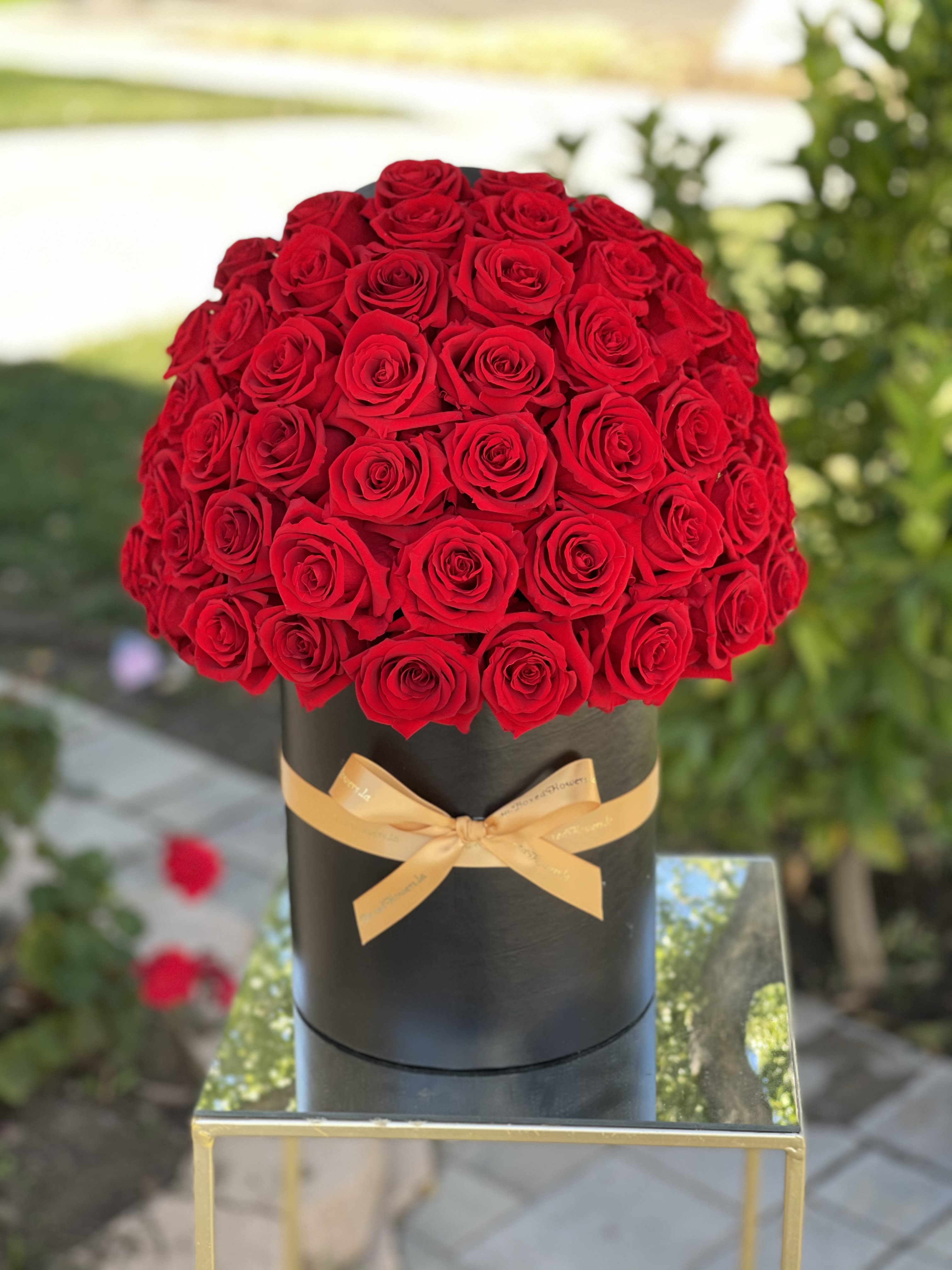 Round bouquet of red roses in a black box with a gold ribbon
