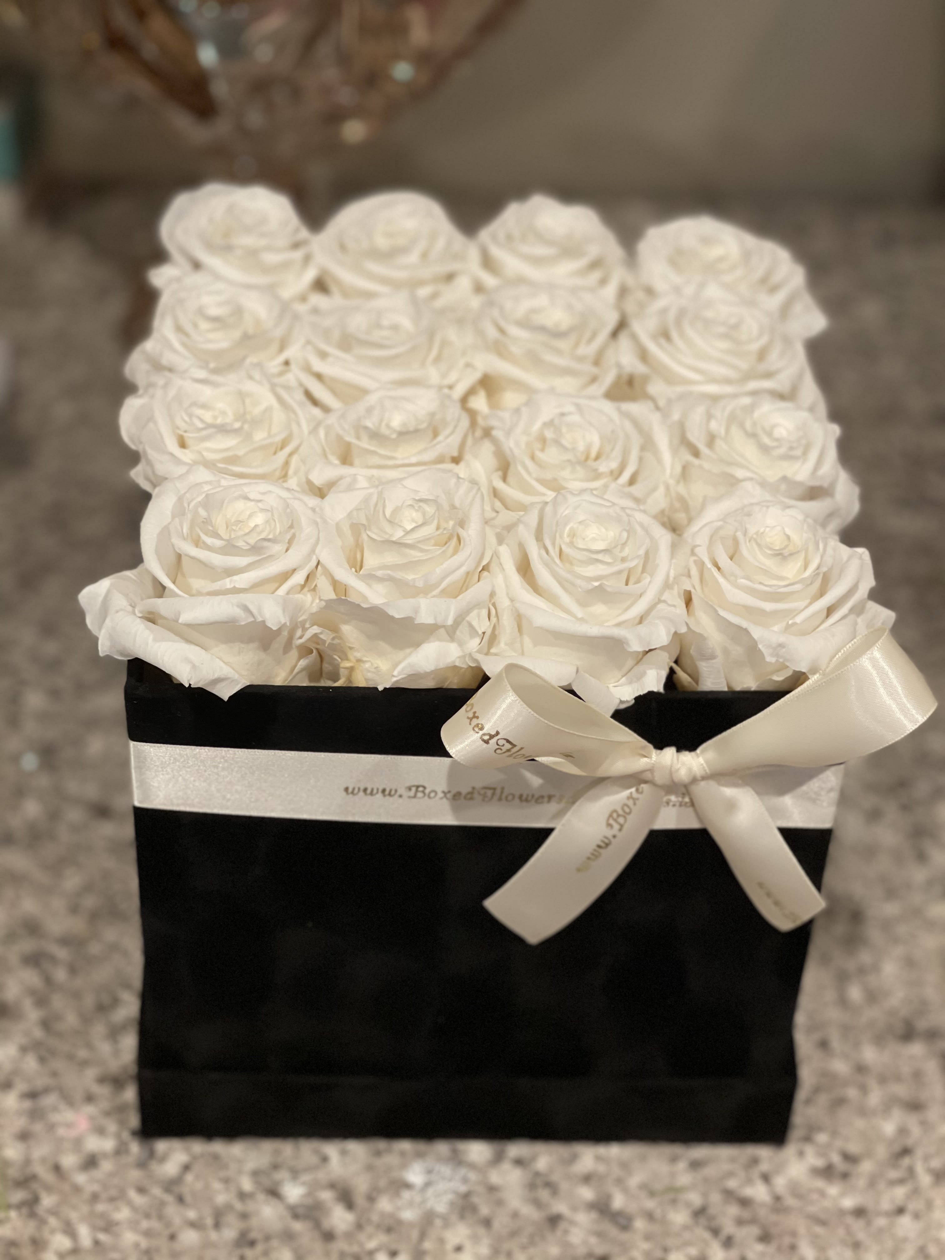 White roses arranged in a black box with a satin ribbon bow
