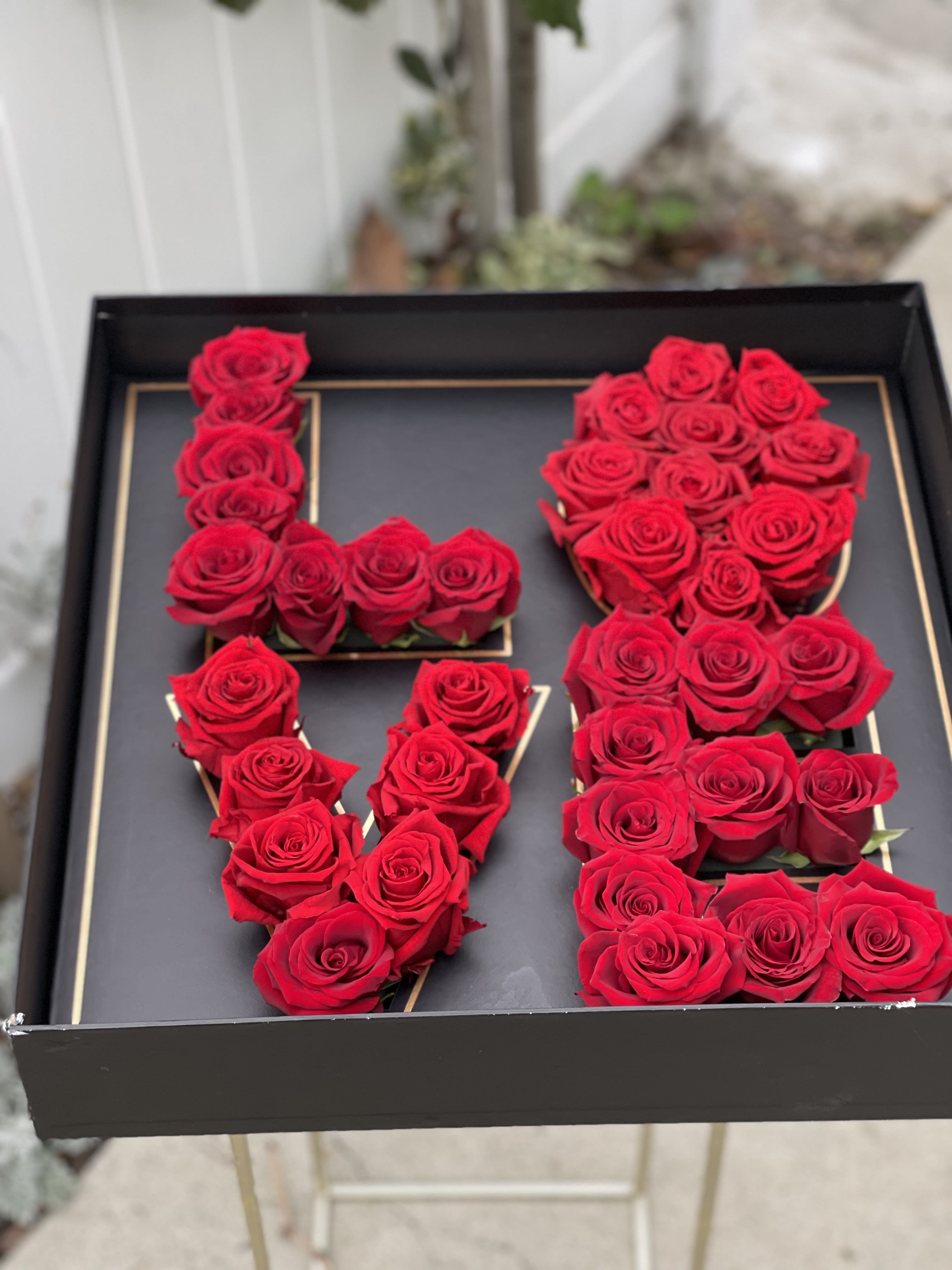 Red roses arranged in the shape of the letters L, O, V, and E in a black box