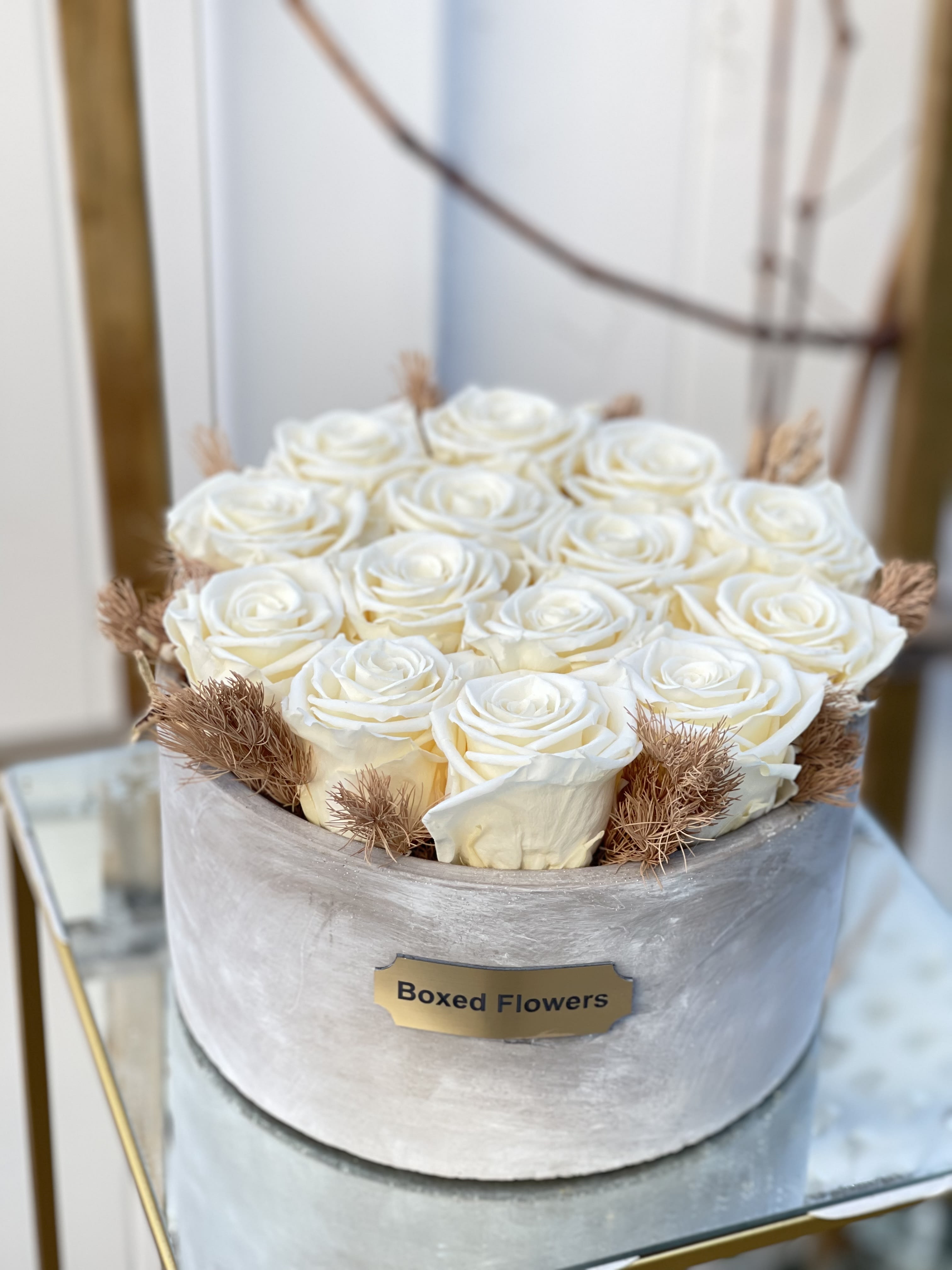 White roses arranged in a round box with dried accents