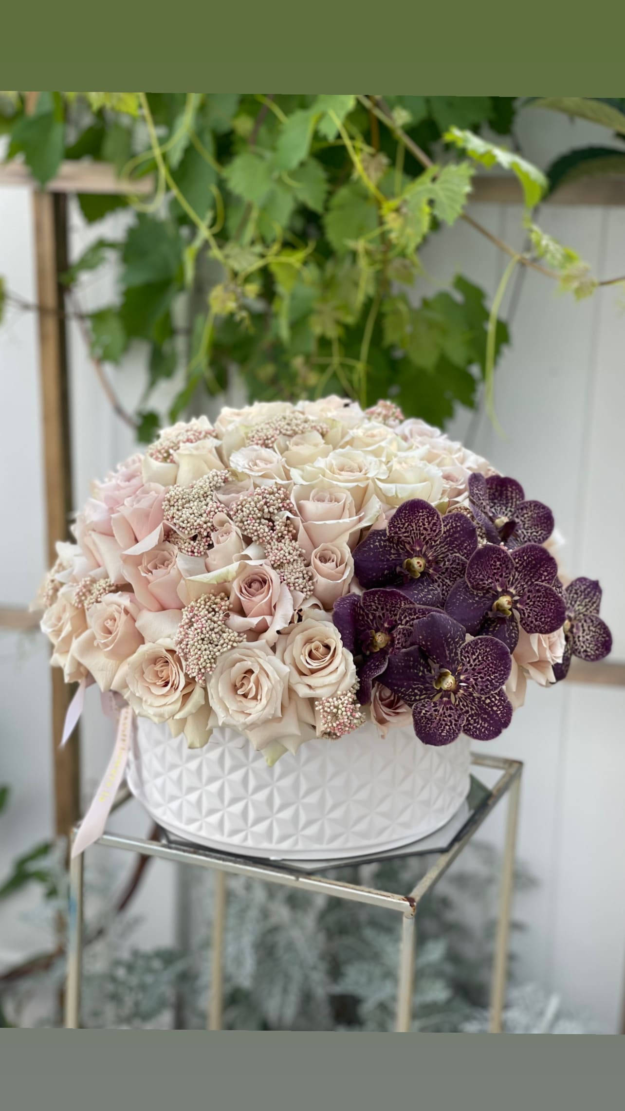 Round bouquet of pale roses and purple orchids in a white textured box