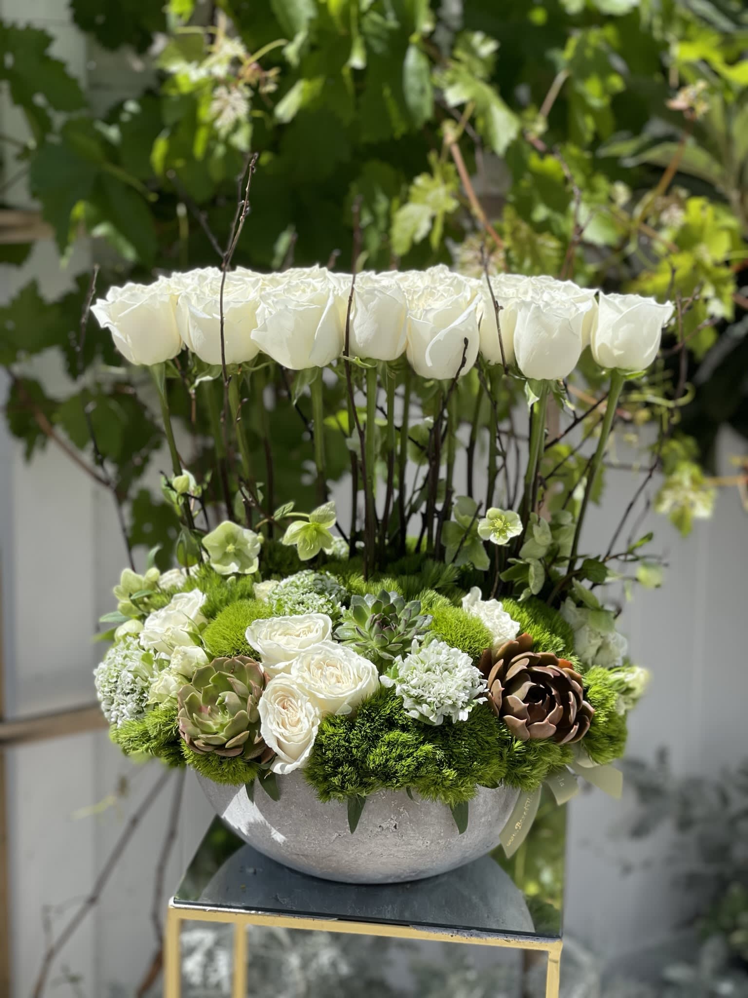 White roses and green succulents in a round gray vase