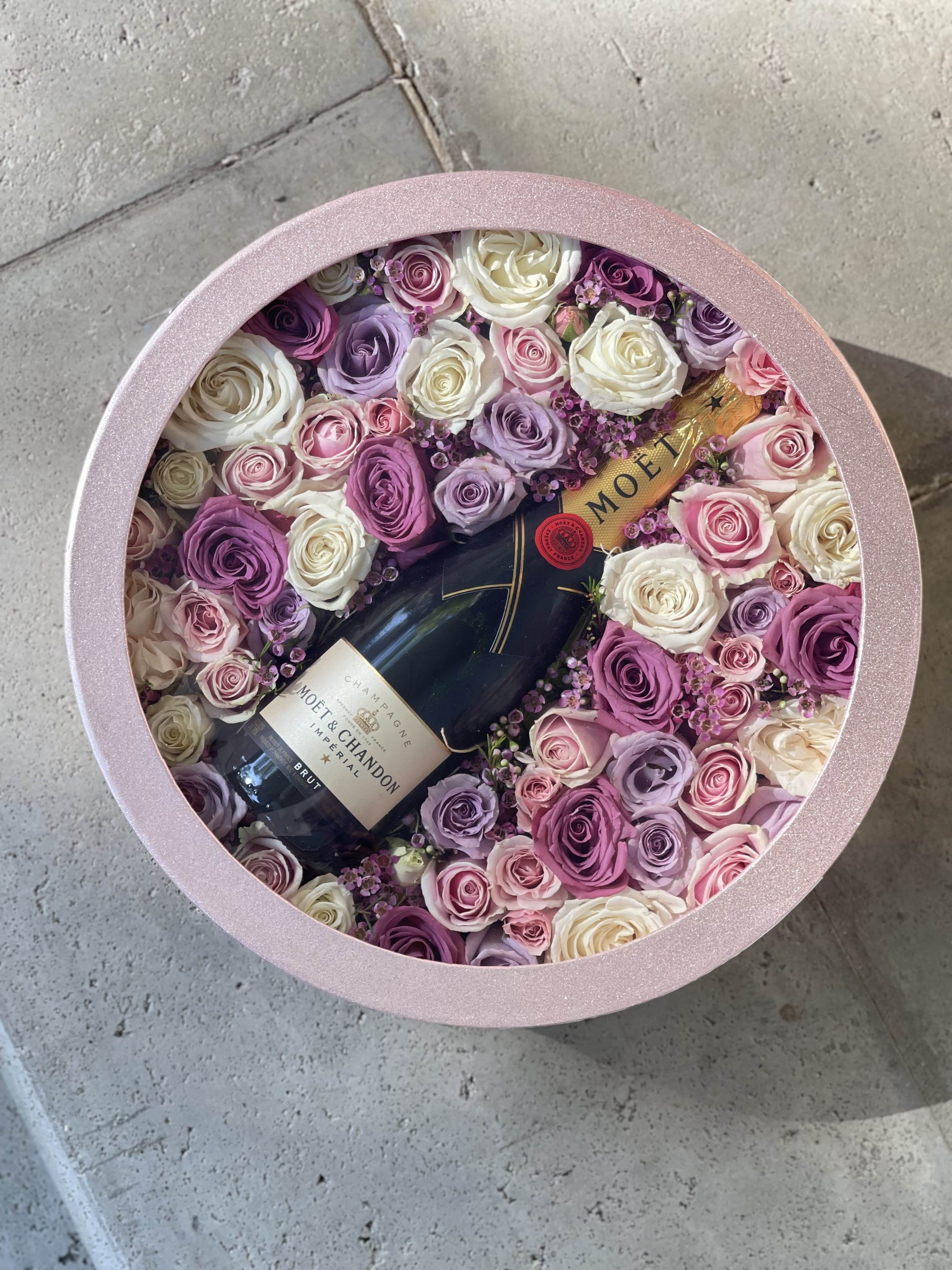 Round pink box filled with roses and a champagne bottle