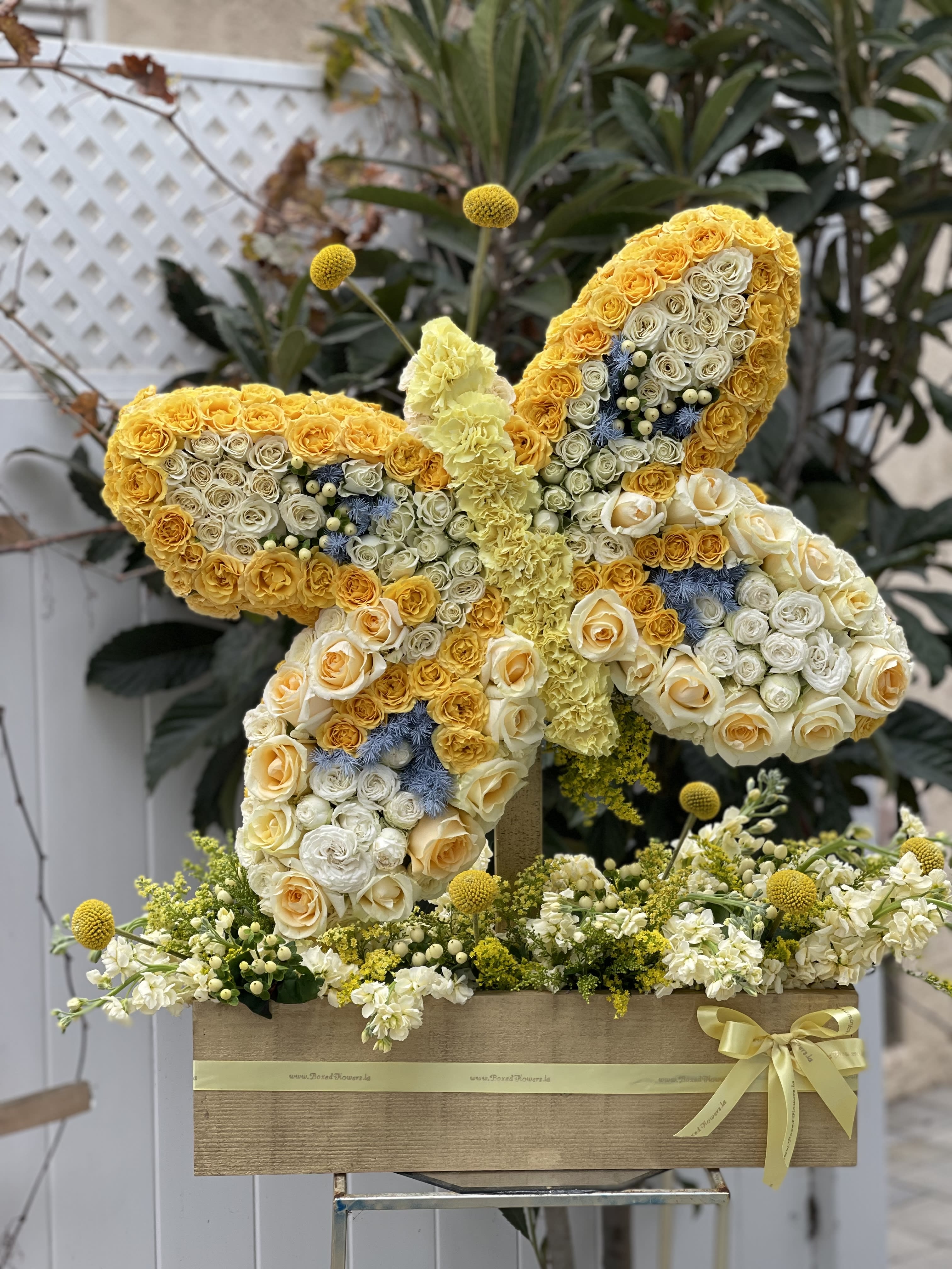 Butterfly-shaped floral arrangement of yellow and white roses with blue accents
