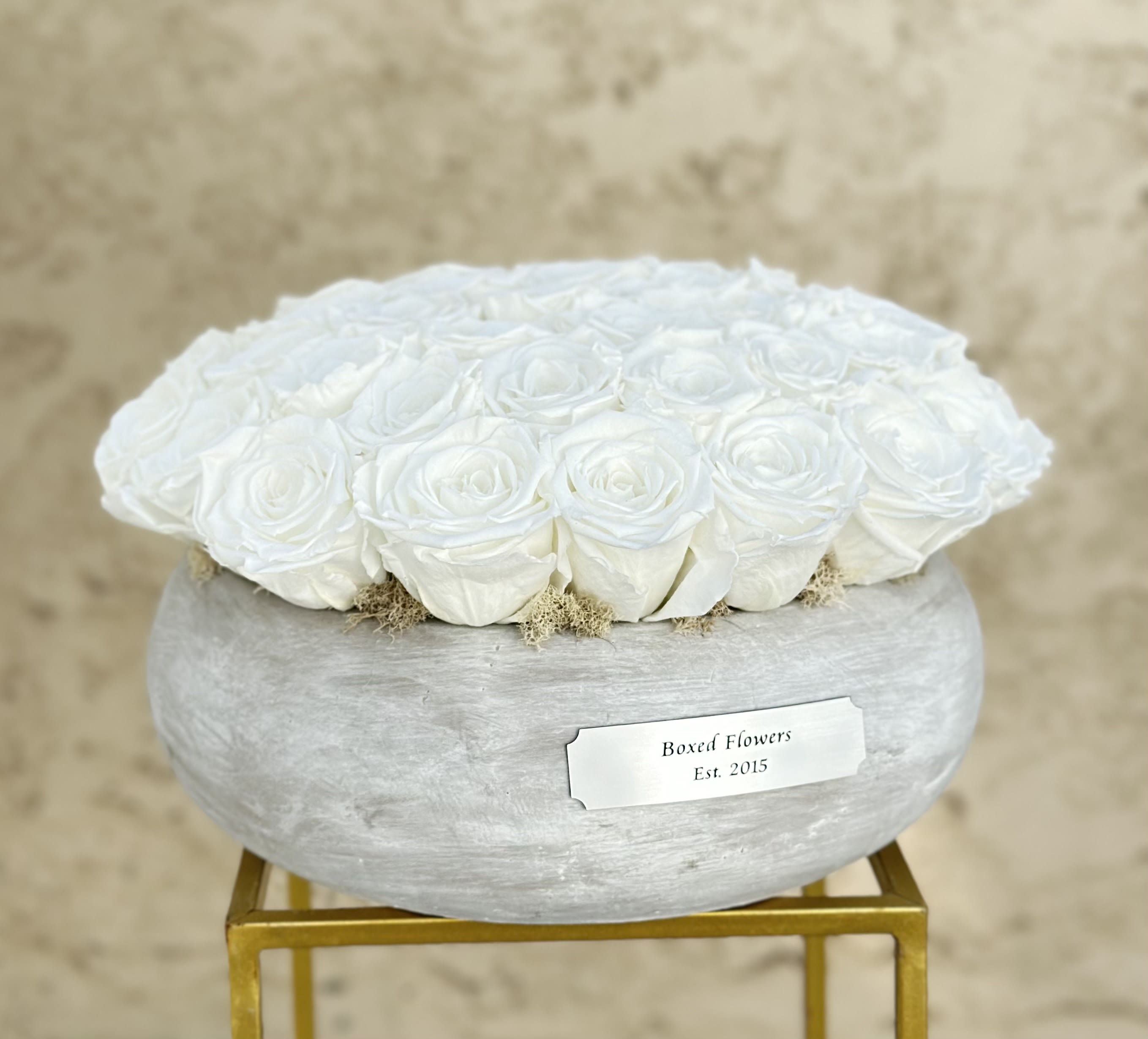 White roses arranged in a round gray box on a gold stand