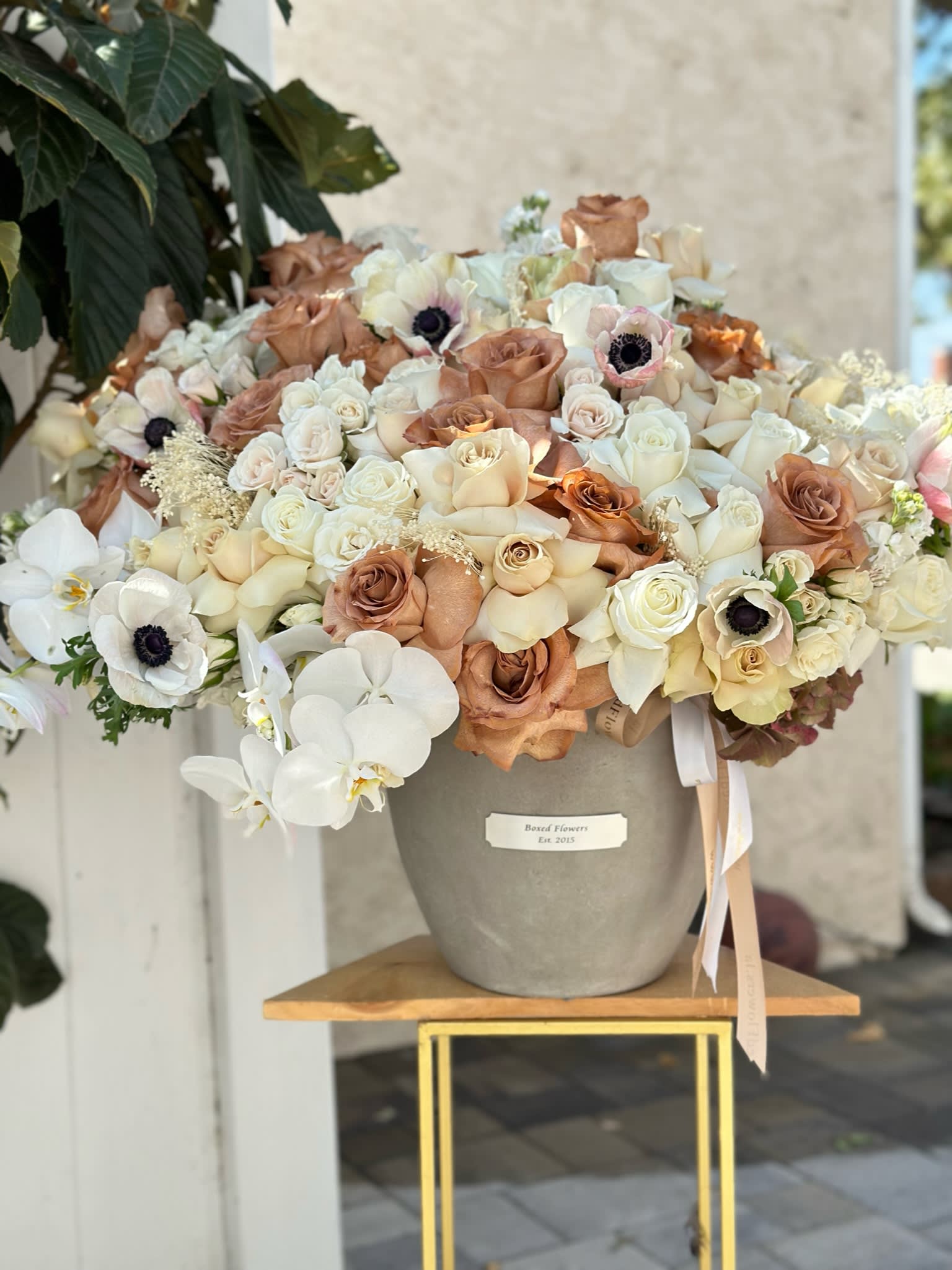 Large bouquet of cream and tan roses with white orchids in a gray vase