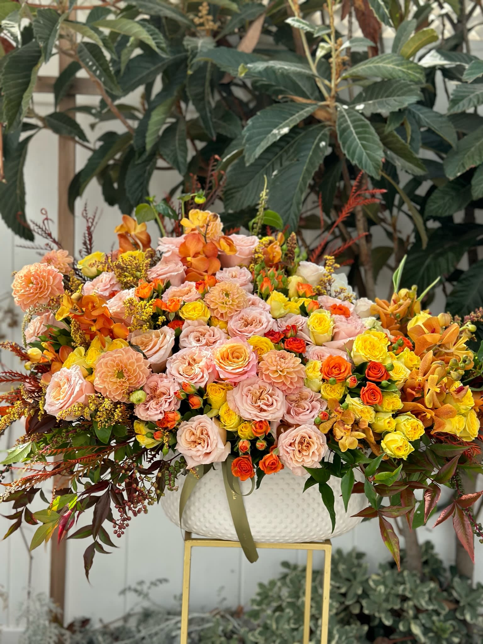 Large mixed floral arrangement in a white bowl vase with pink, yellow, and orange blooms
