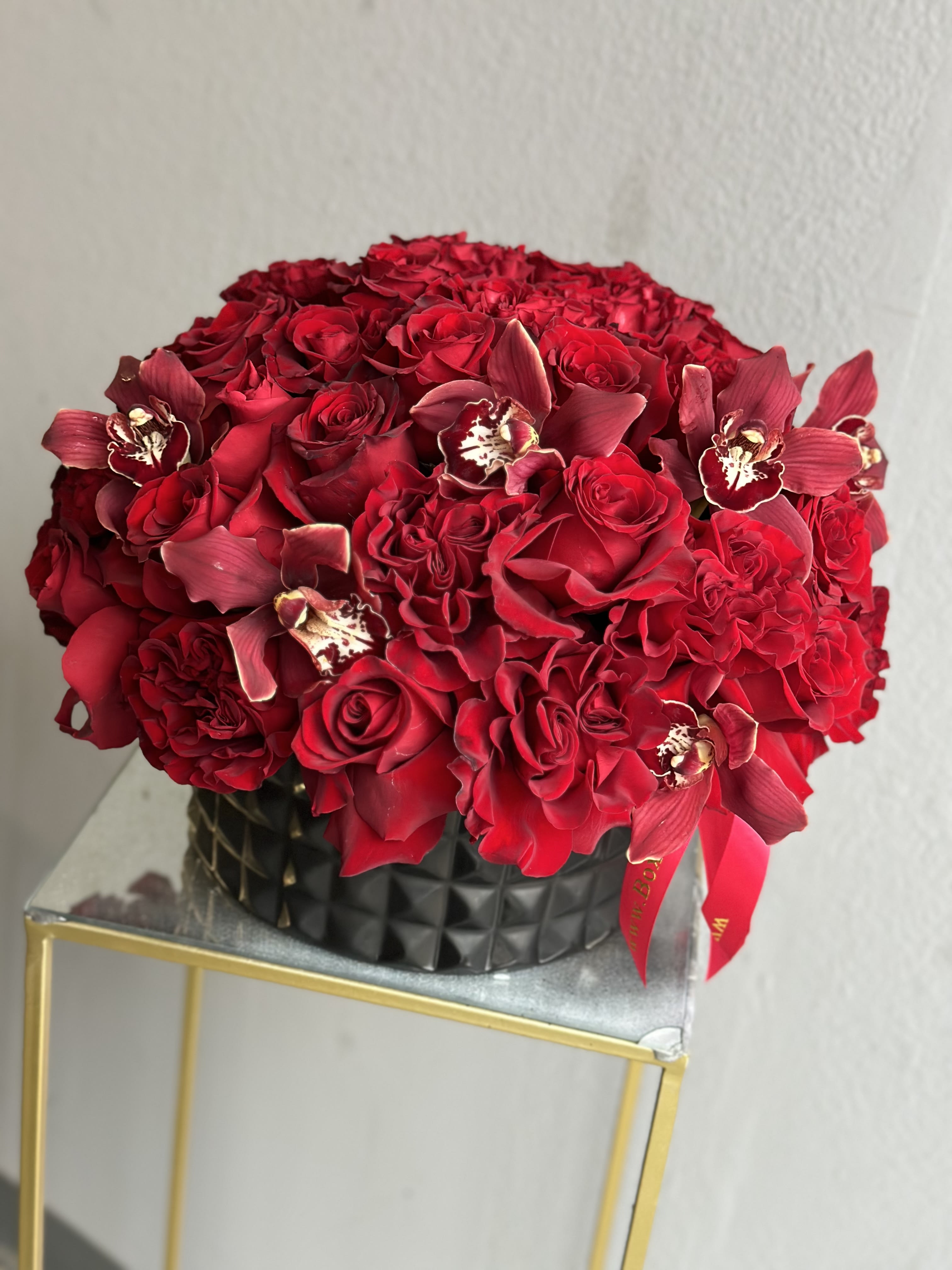 Red rose bouquet with burgundy orchids in a black vase