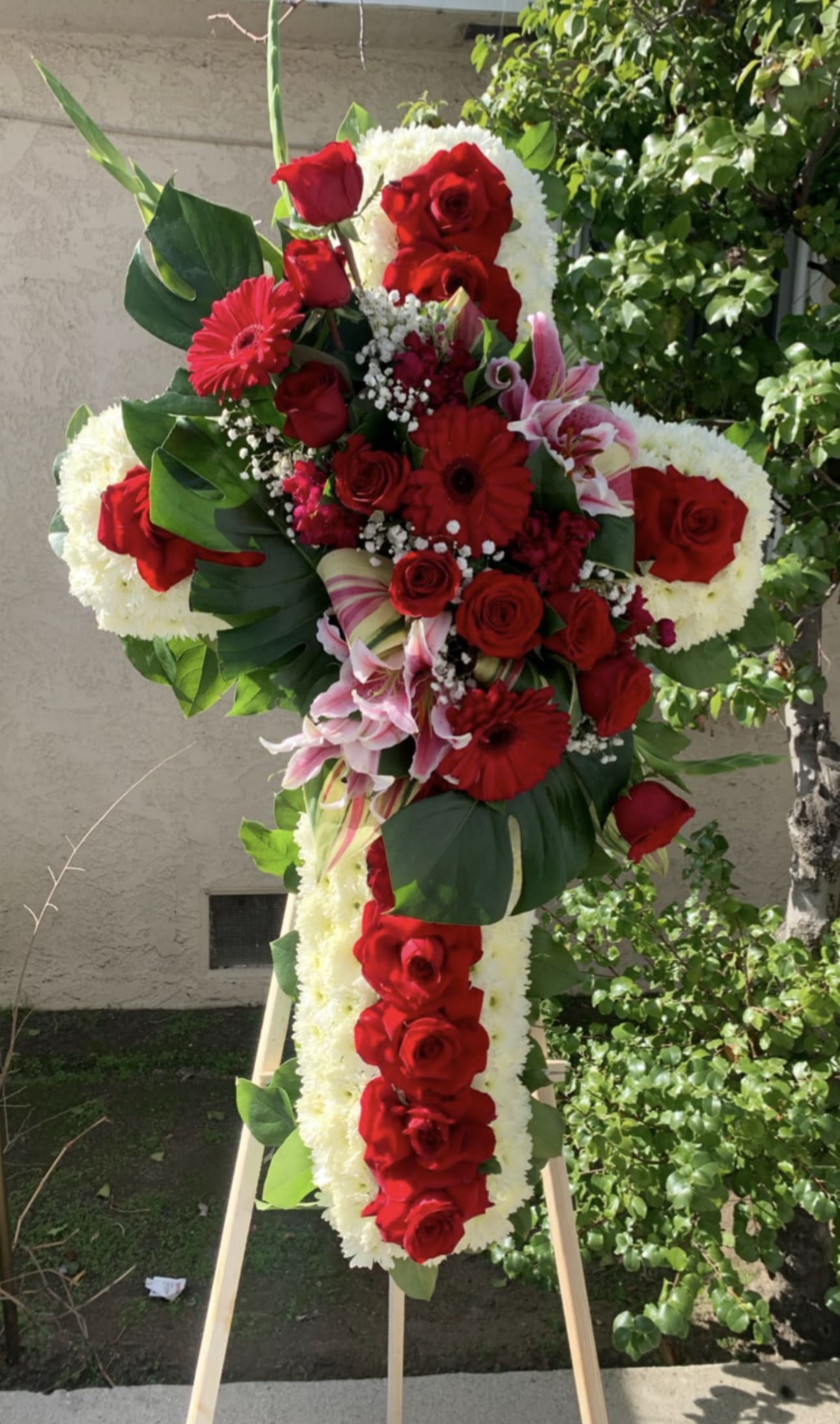 Standing floral cross with red roses and white flowers on an easel