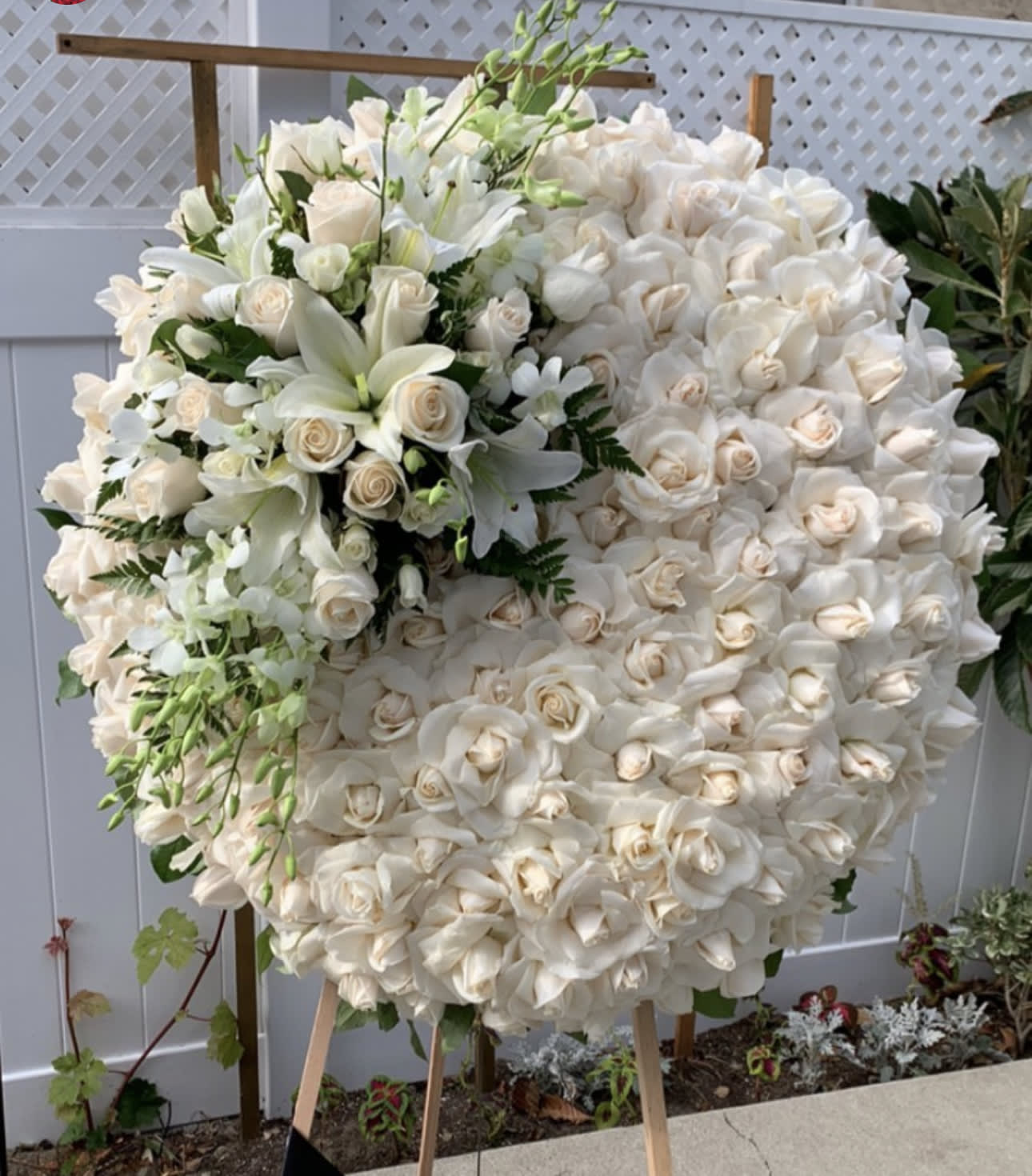 Large white floral wreath on an easel with roses and lilies