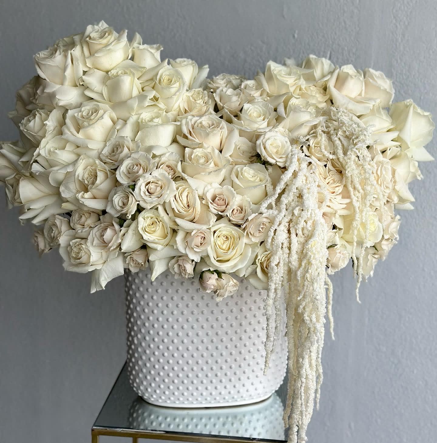White rose arrangement in a textured white vase with trailing white accents