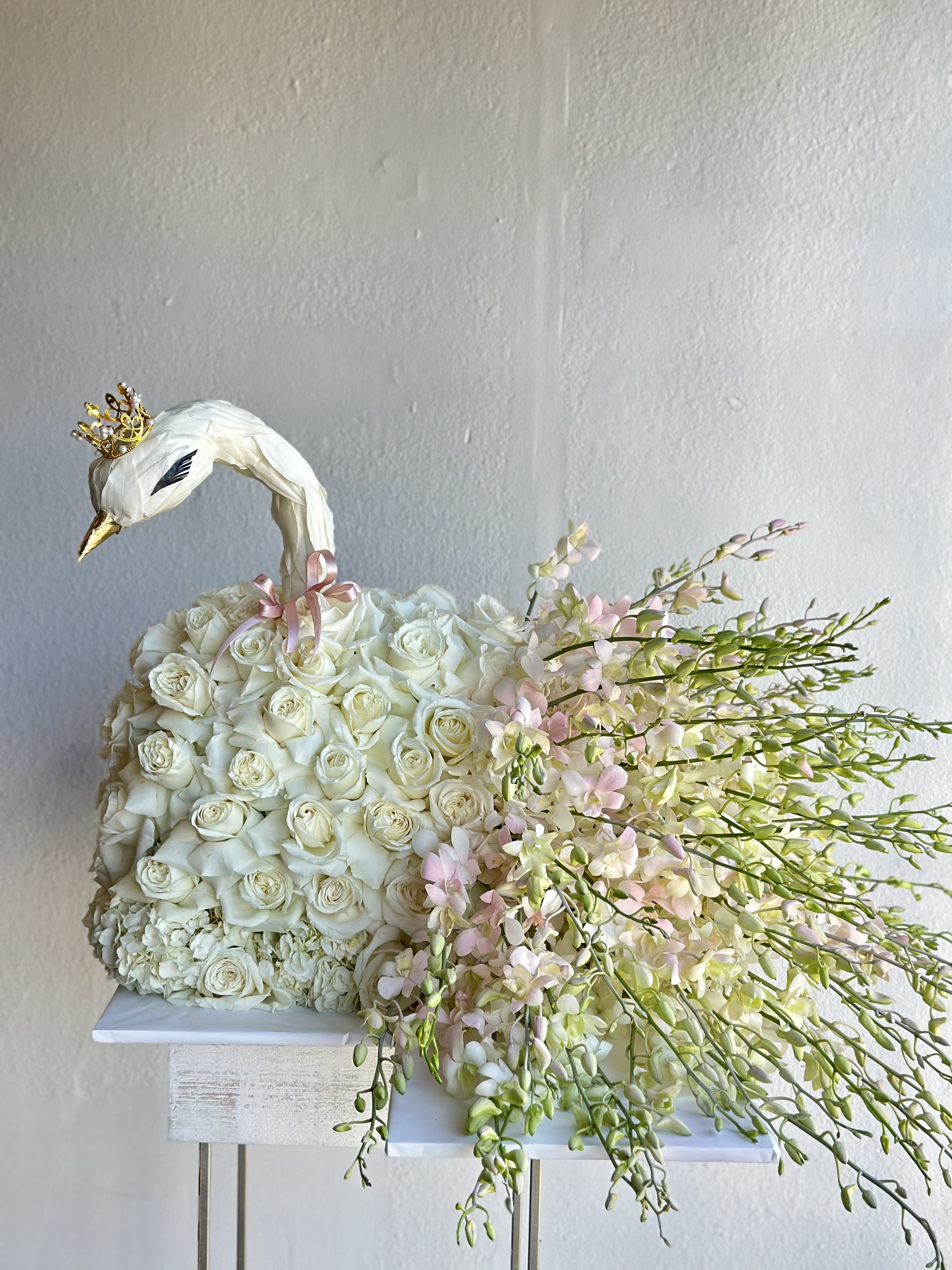White rose arrangement shaped like a swan with pink orchid sprays