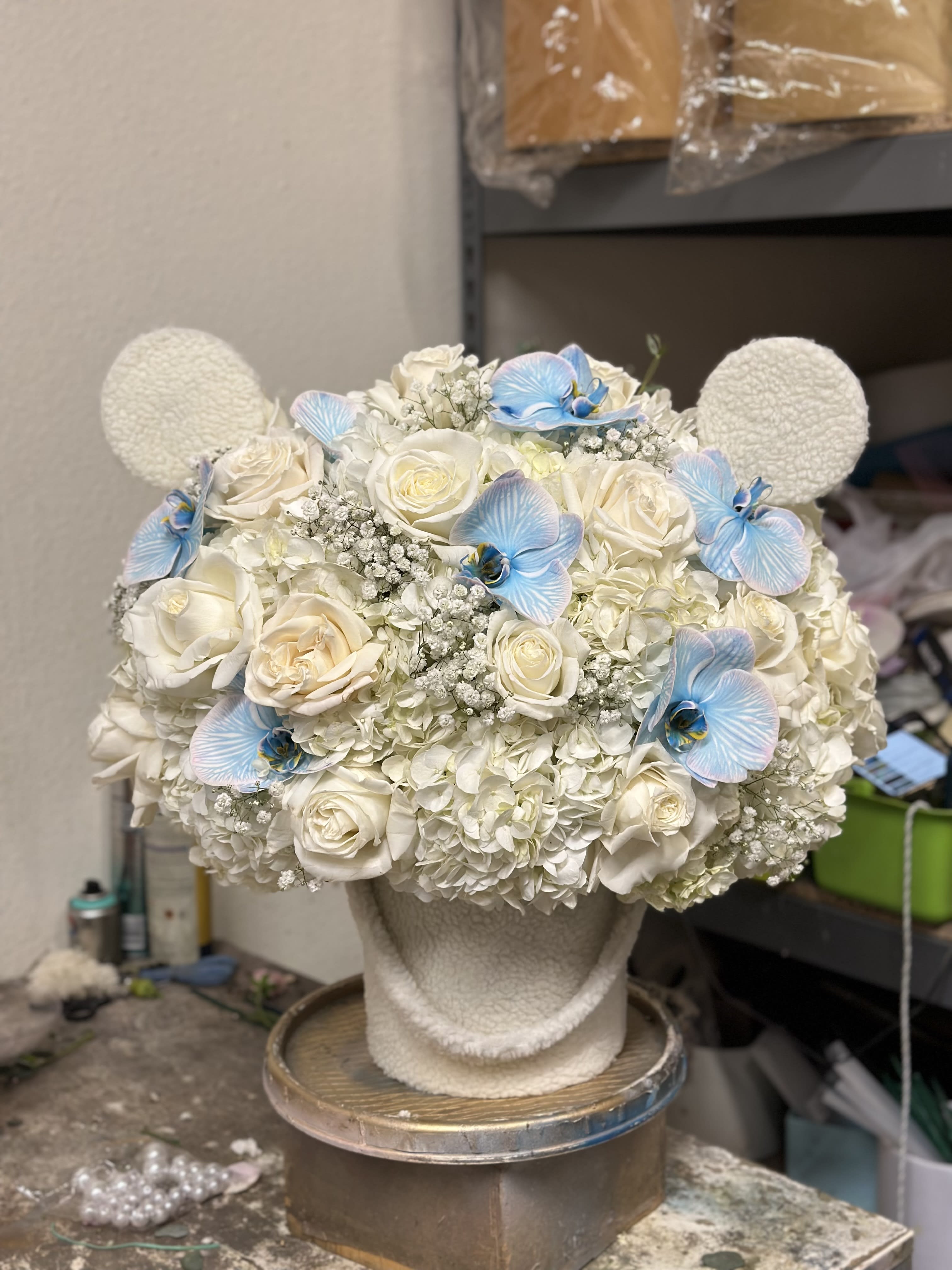 White floral arrangement with blue orchid accents on a textured stand