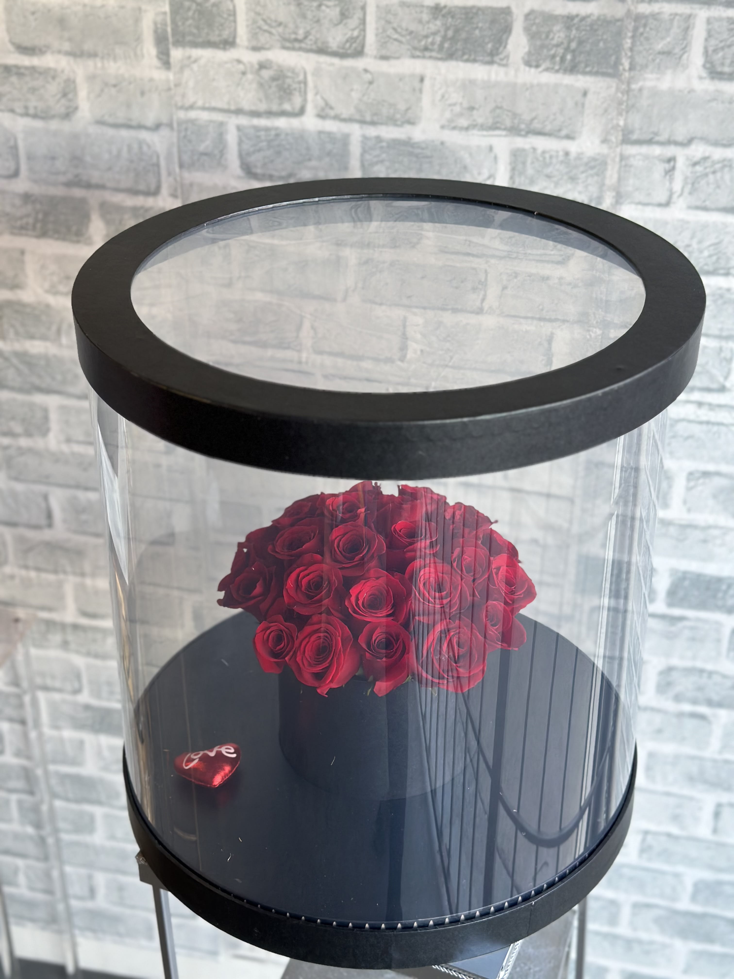 Red roses arranged in a black round box with a clear lid