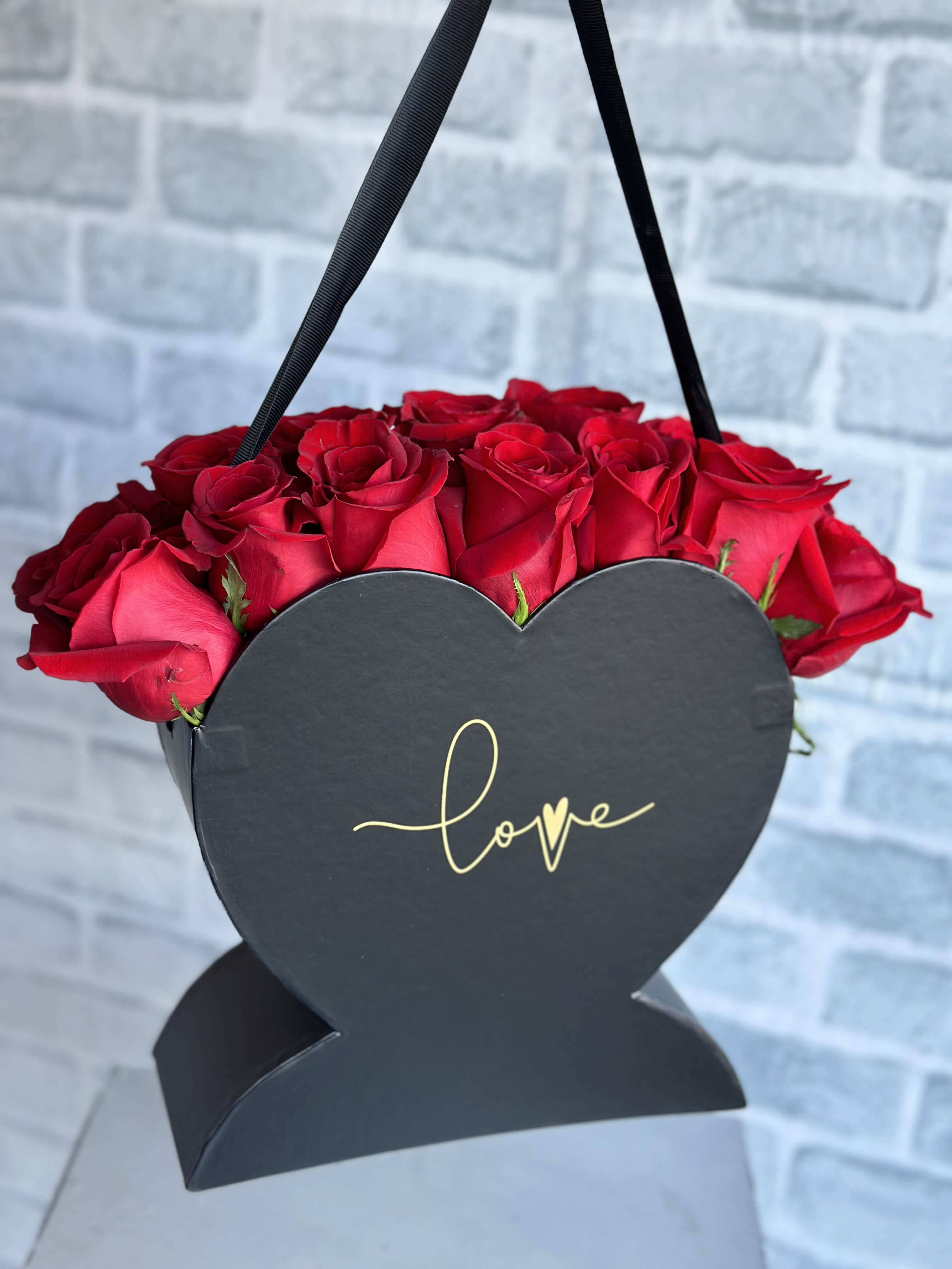Red roses in a black heart-shaped box with a "love" label