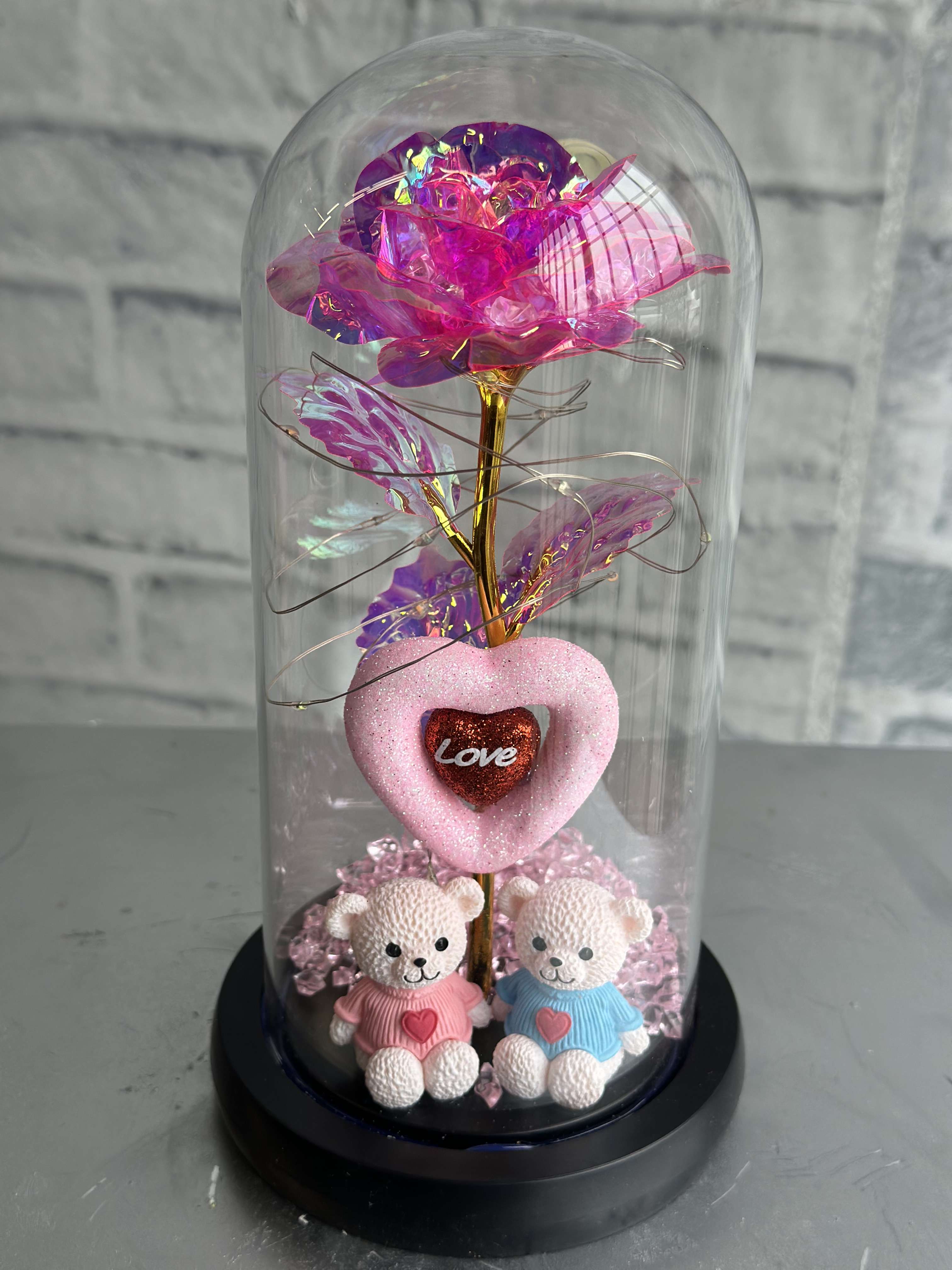 Pink iridescent artificial rose under a glass dome with two teddy bears