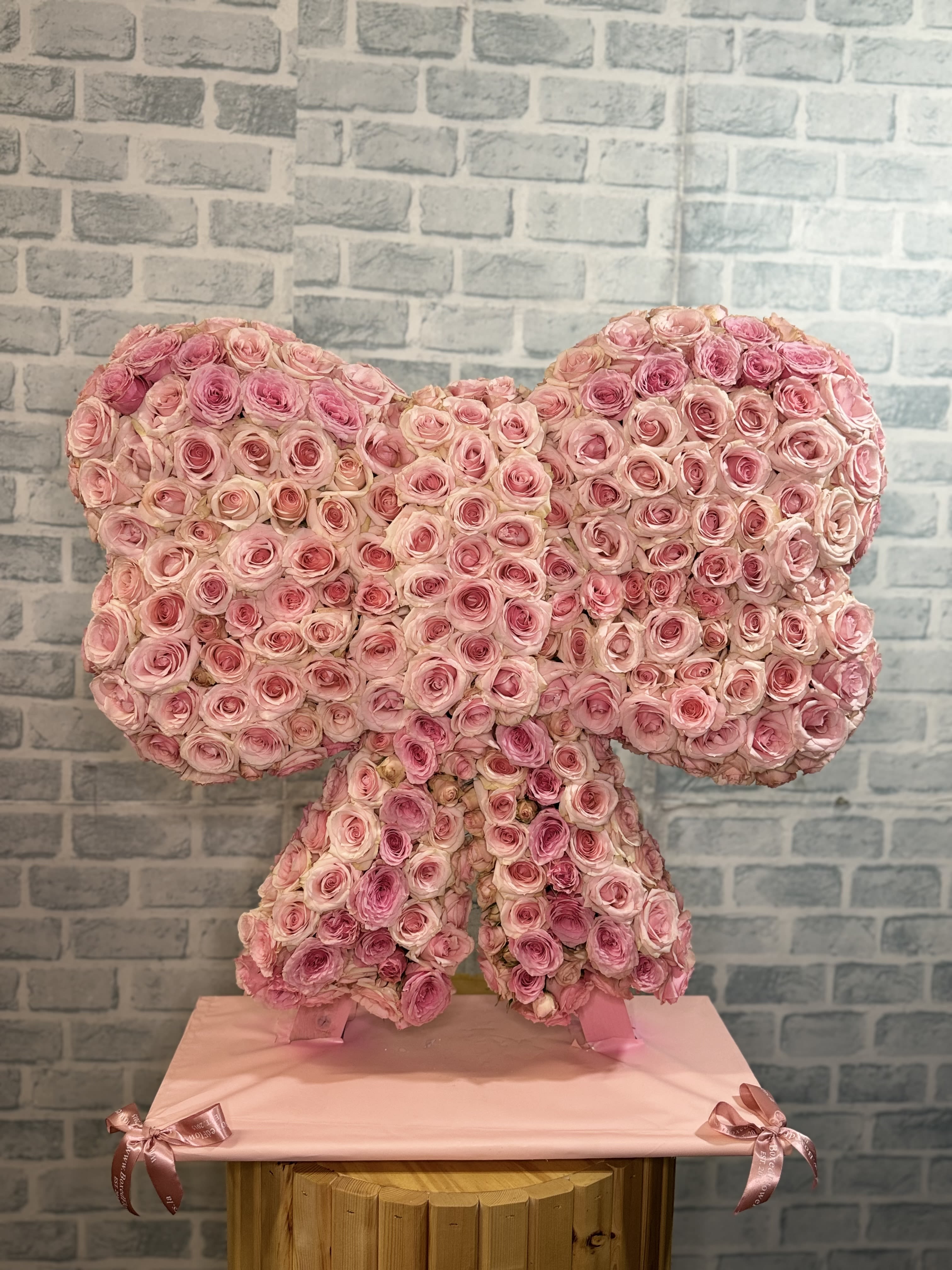 Pink rose arrangement shaped like a bow on a pedestal