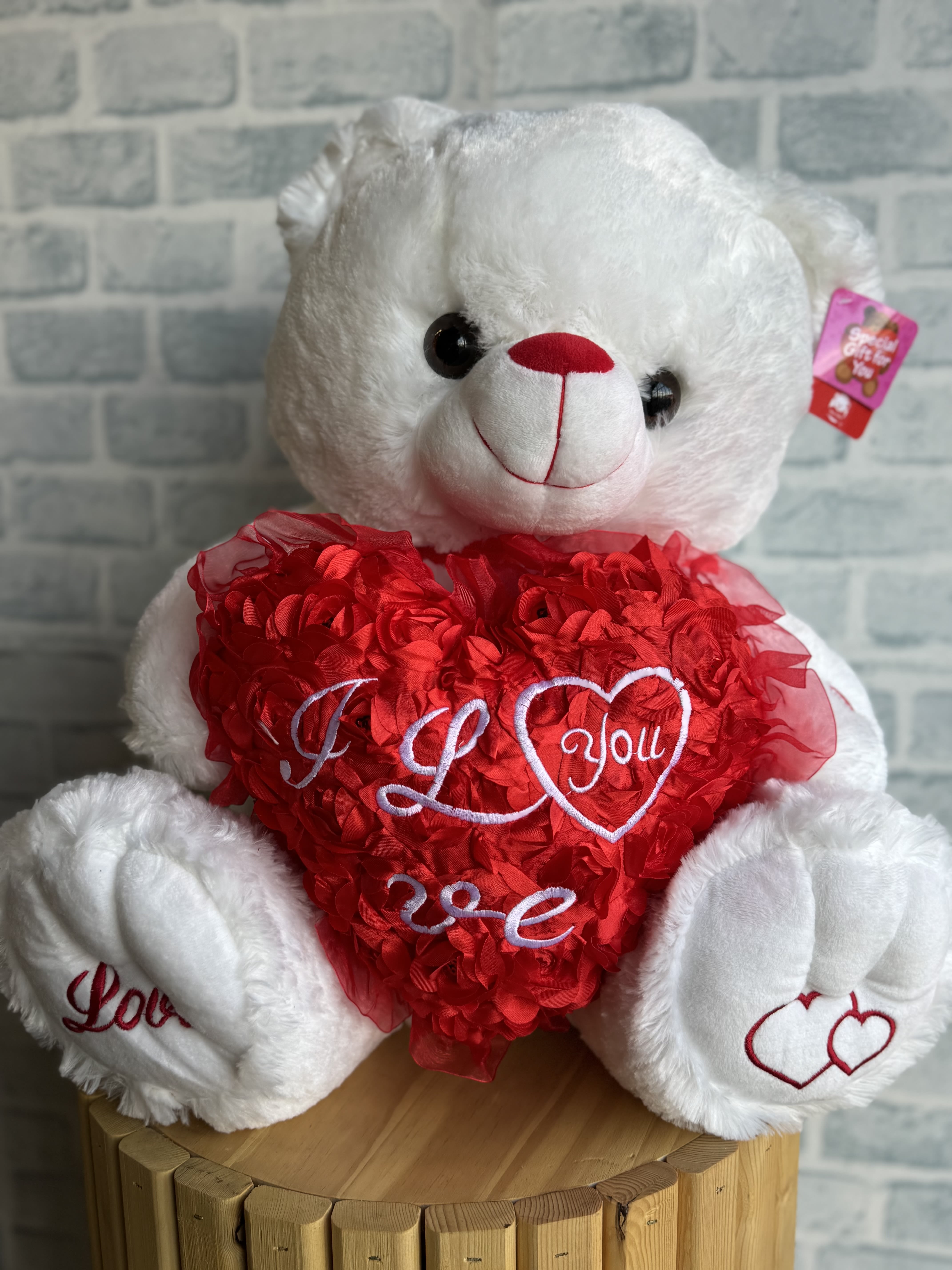 White teddy bear holding a red heart with embroidered love text