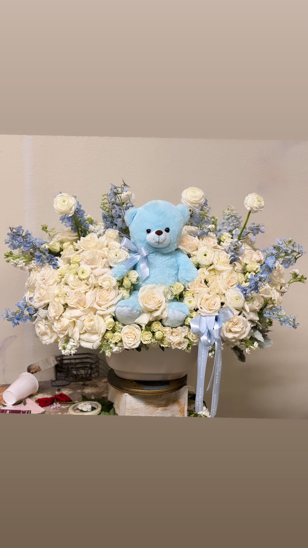 Blue teddy bear in a white rose and blue flower arrangement