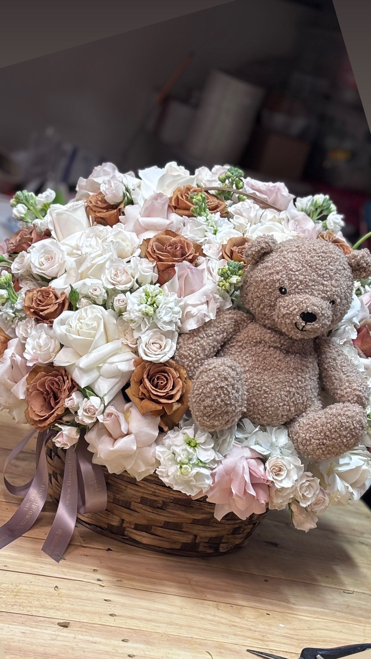 Basket arrangement of white and blush flowers with a teddy bear