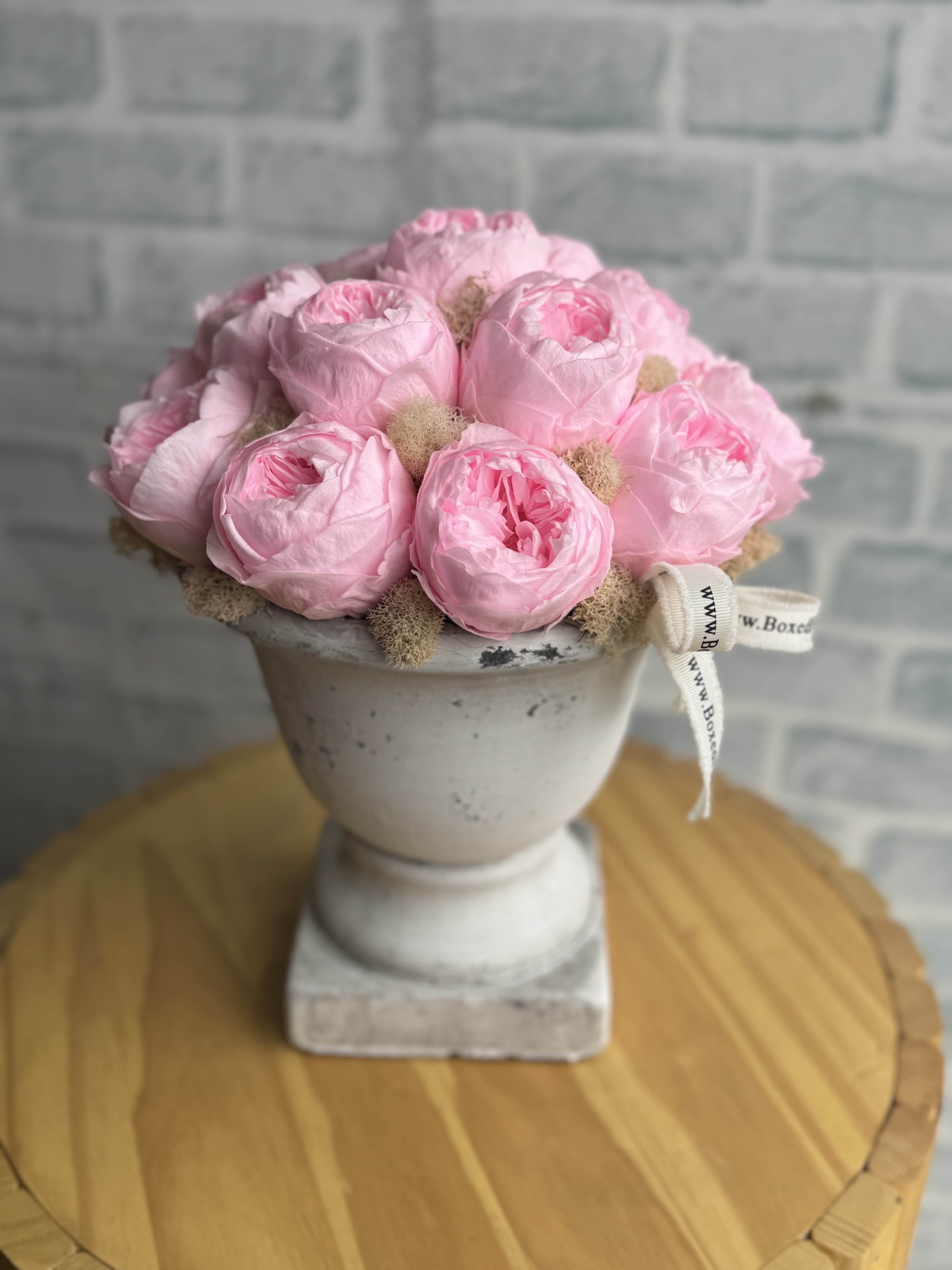 Pink roses arranged in a white pedestal vase with a ribbon bow