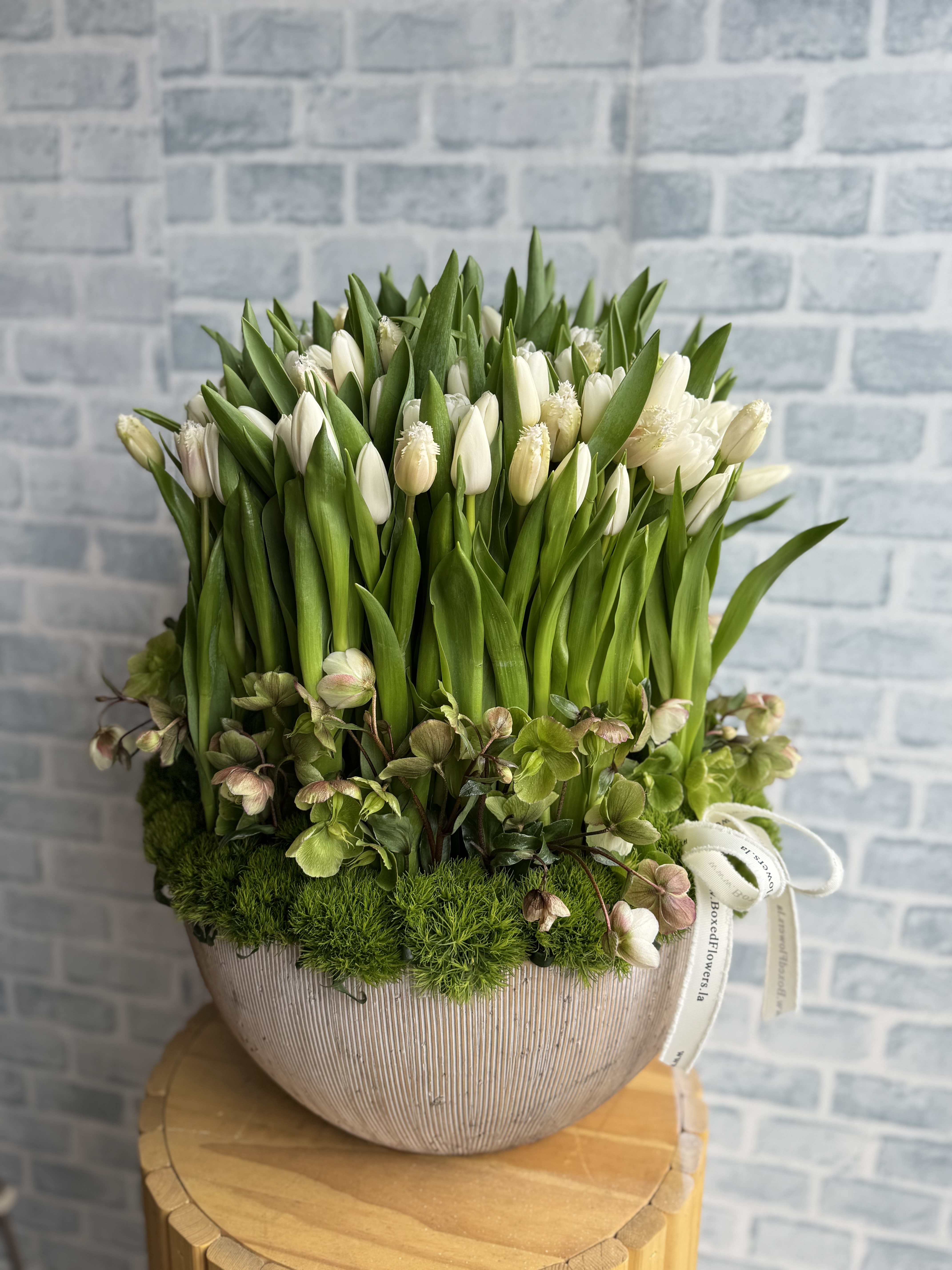 White tulips in a ribbed ceramic vase with moss and hellebore accents