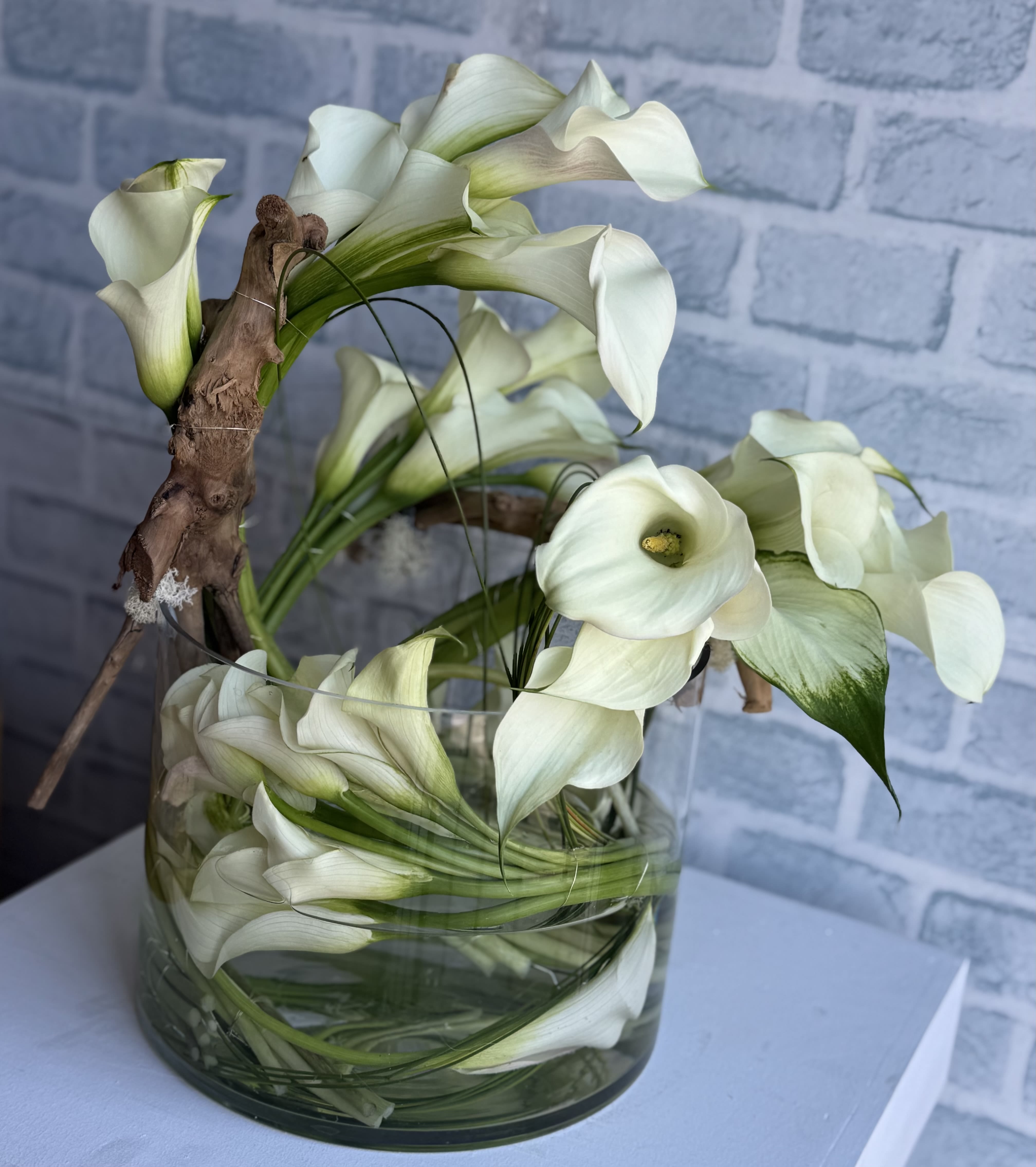 White calla lilies arranged in a glass vase with a branch accent