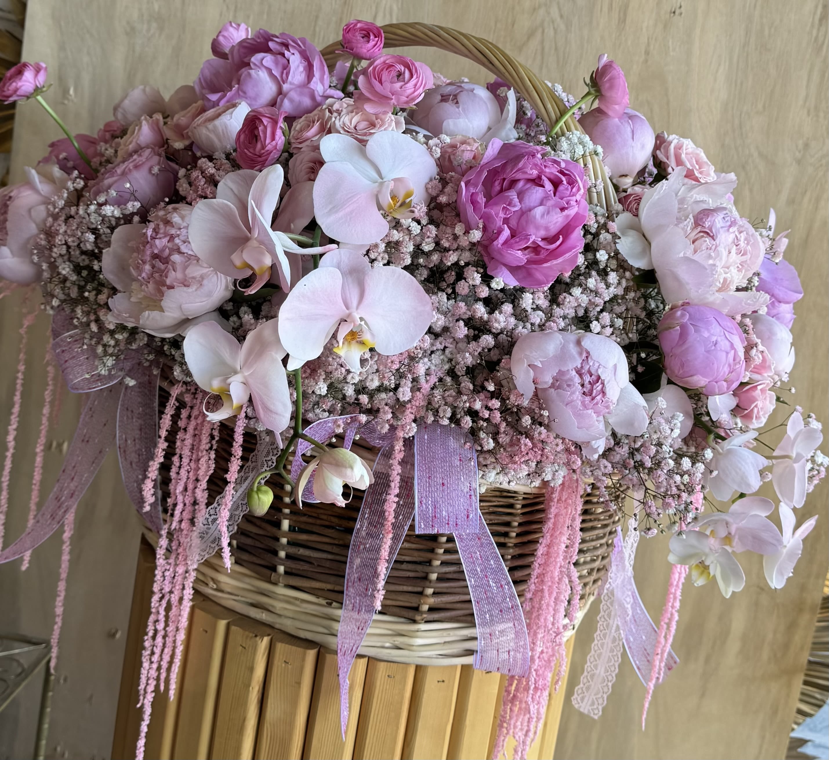 Pink floral arrangement in a wicker basket with orchids and peonies